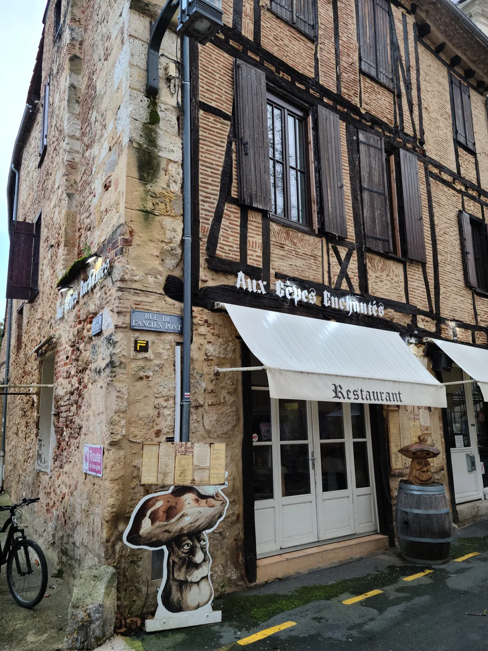 Aux Crêpes Enchantées restaurant in Bergerac's old town, a half-timbered stone building with a white awning and a decorative chef figure at the entrance