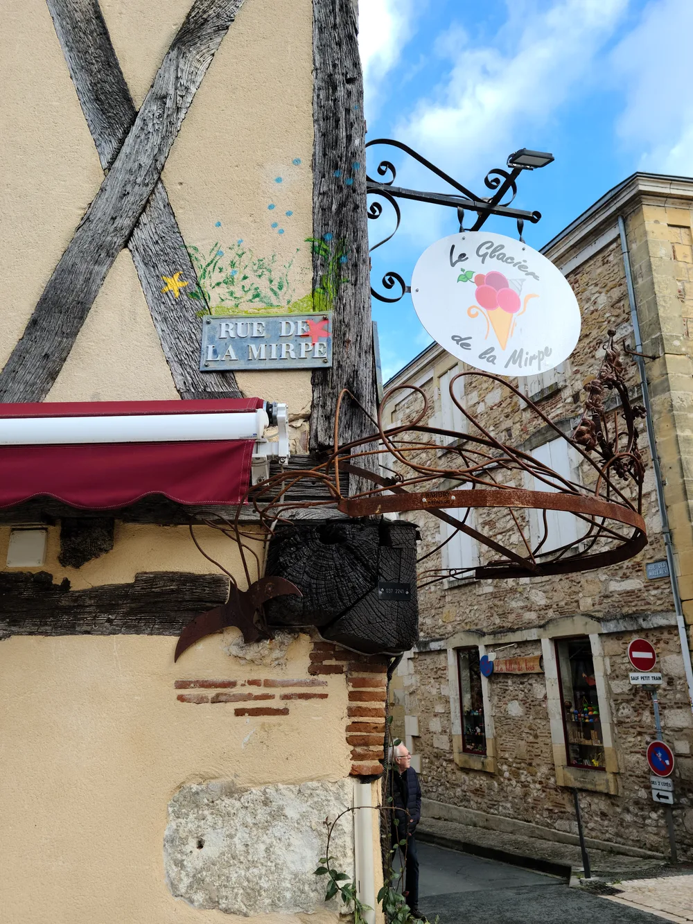 La Glacière ice cream shop sign on an iron bracket at a corner in Bergerac's old town, a half-timbered building behind it and Rue de la Myrpe sign visible