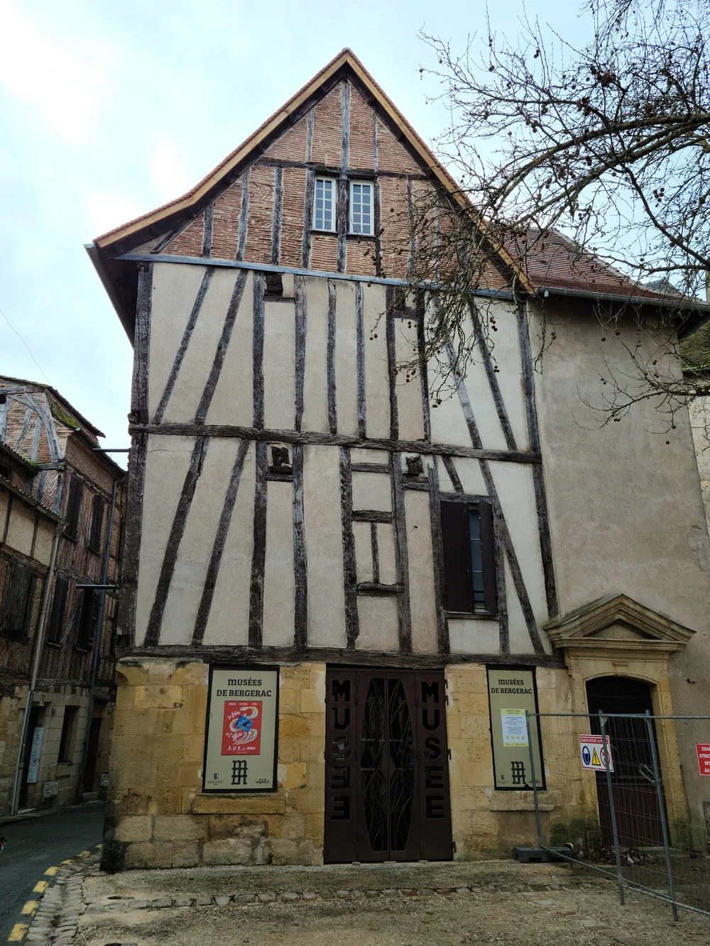 Medieval half-timbered building in Bergerac's historic center with dark timber frame and cream plaster infill, museum signs at street level