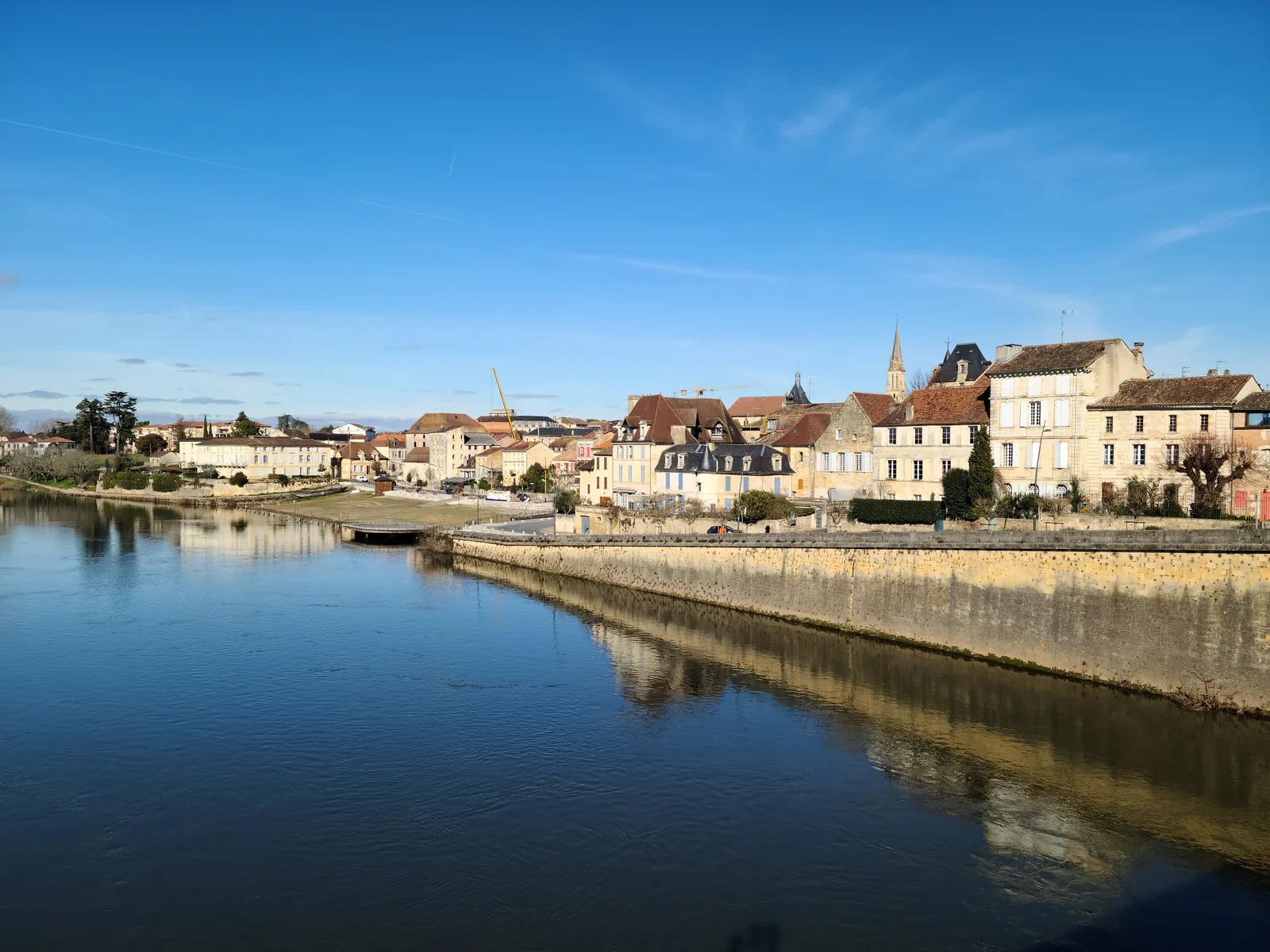 Bergerac's old town stone quay and church steeple perfectly reflected in the calm Dordogne River on a clear blue winter day