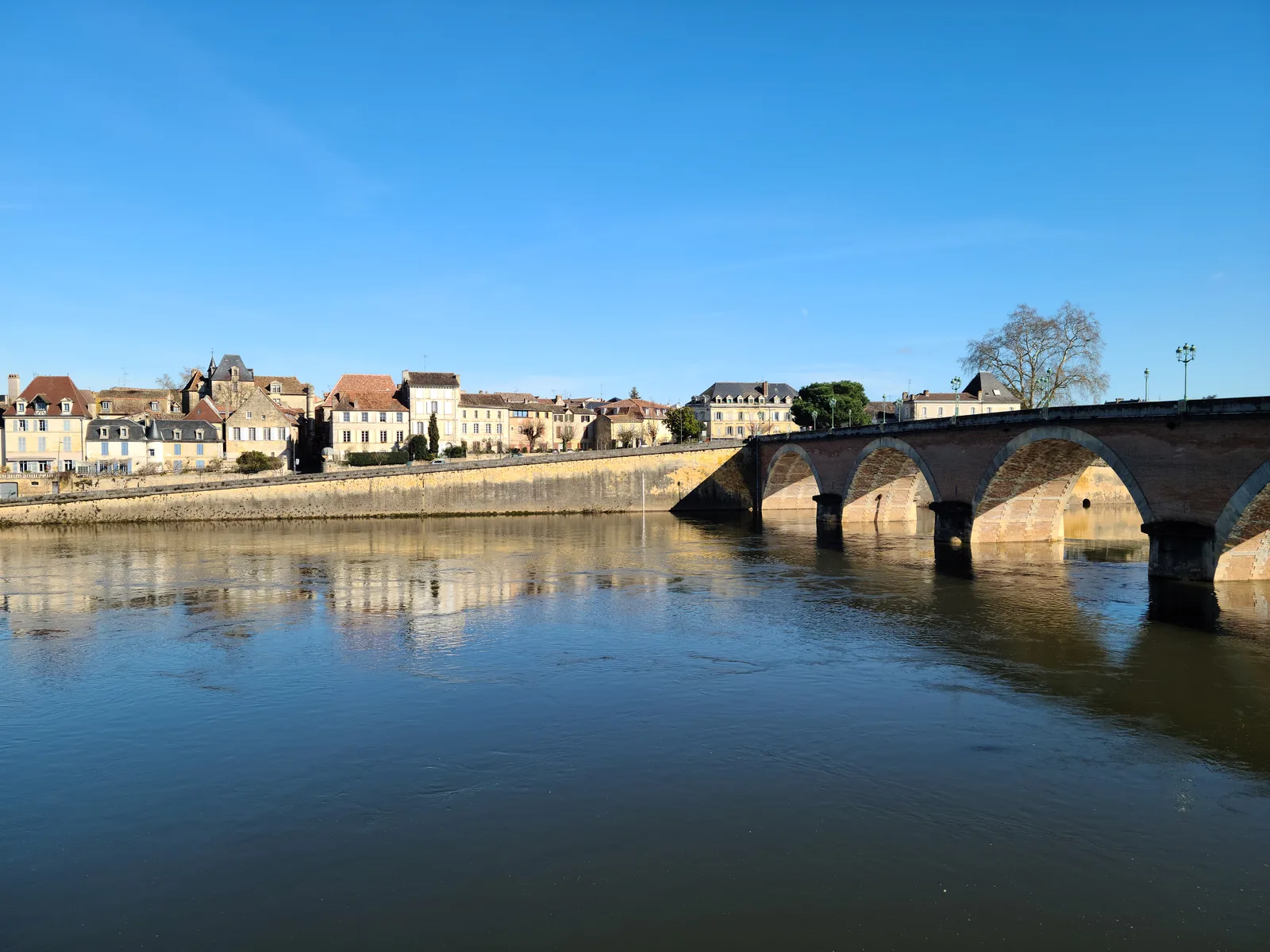 The stone arch Pont Vieux bridge spanning the Dordogne River at Bergerac, old town buildings and church tower lining the north bank under a clear blue sky