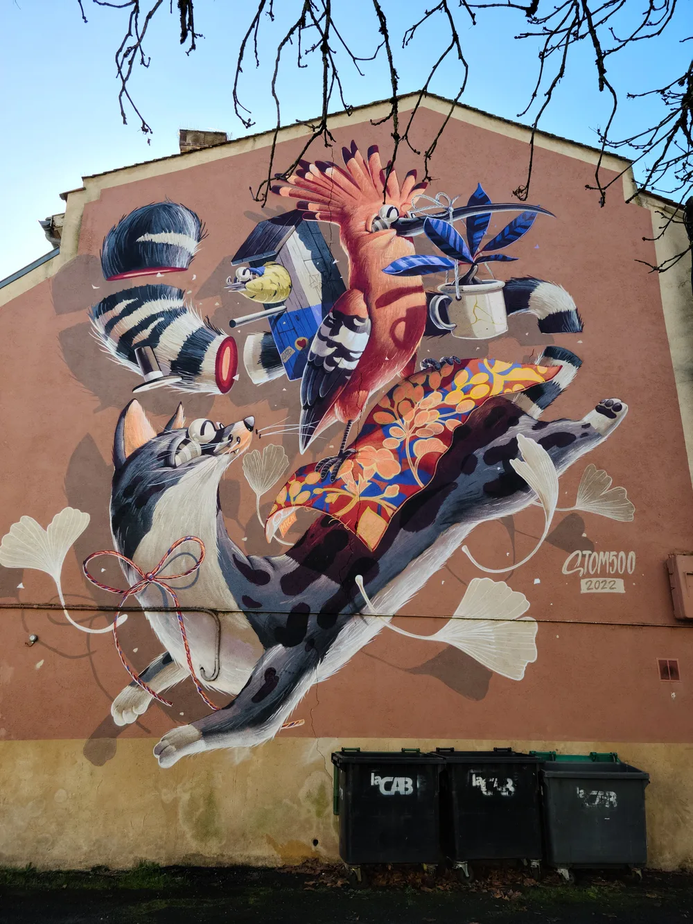 Large colorful street art mural on a building wall in Bergerac featuring a raccoon amid vibrant blue, red, and orange abstract shapes under bare winter trees