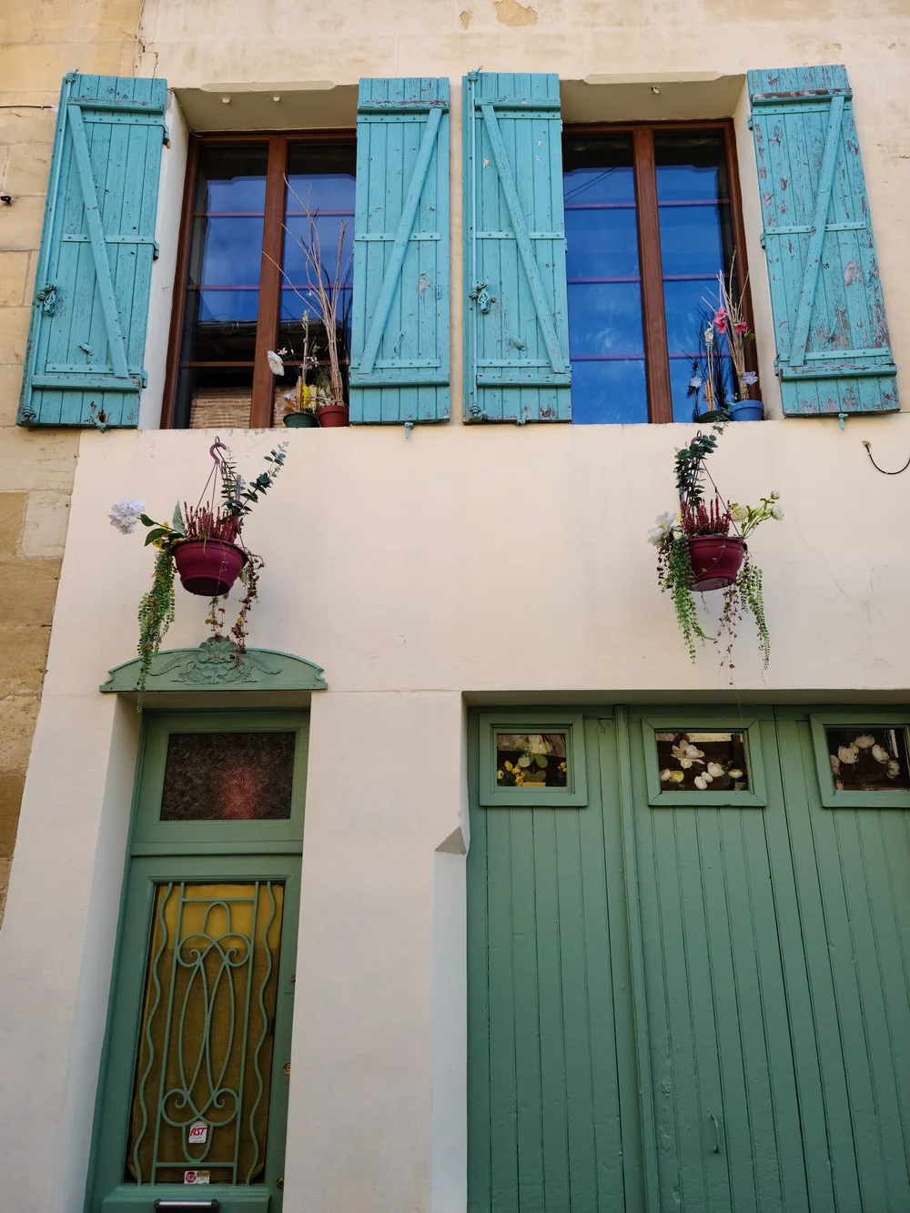 Charming stone building facade in Bergerac's old town with weathered teal-painted shutters and hanging flower baskets on a white plaster wall