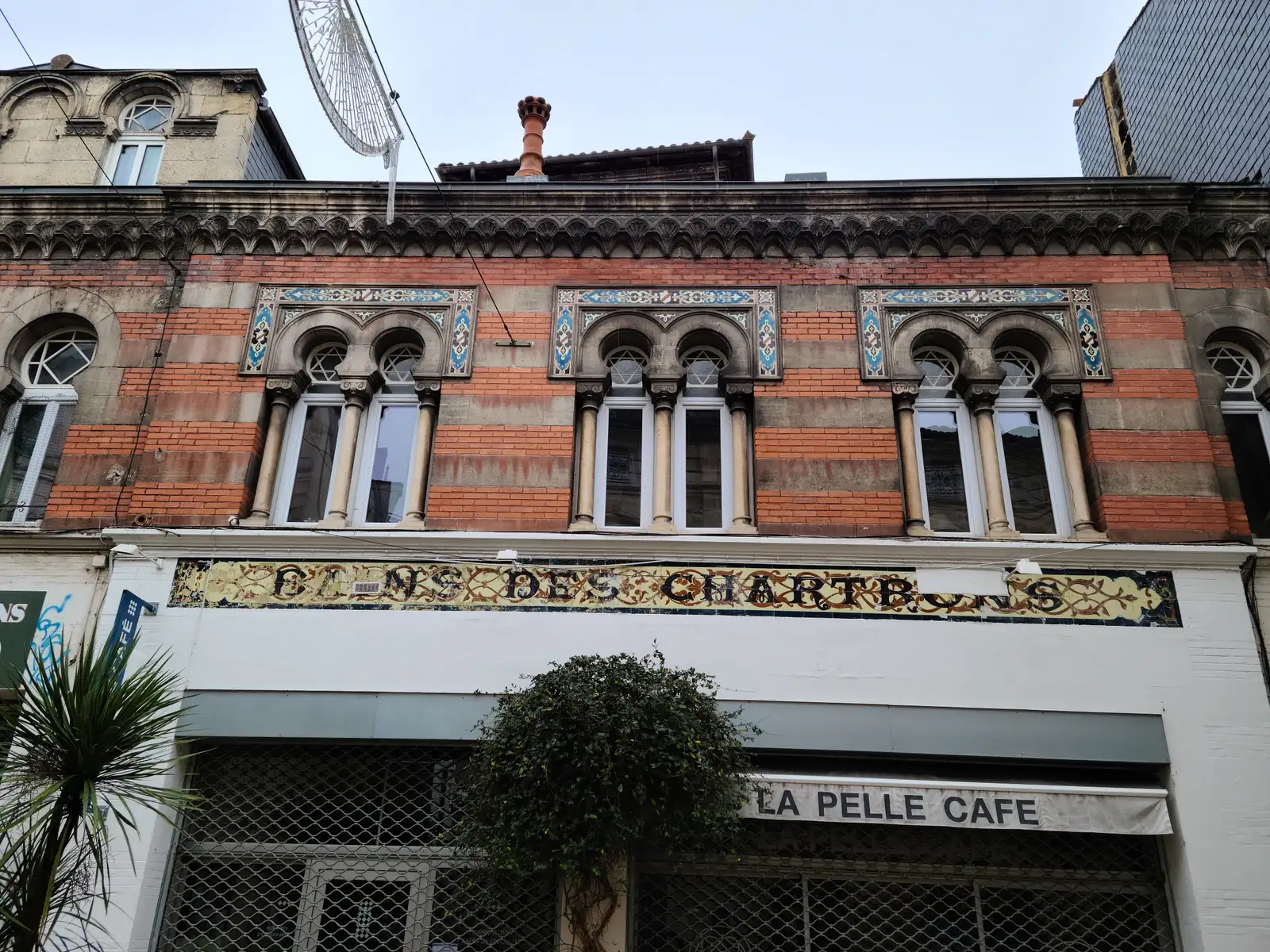 Moorish horseshoe arch windows and gilded mosaic Clos des Chartrons sign above La Pelle Café in Bordeaux's Chartrons district