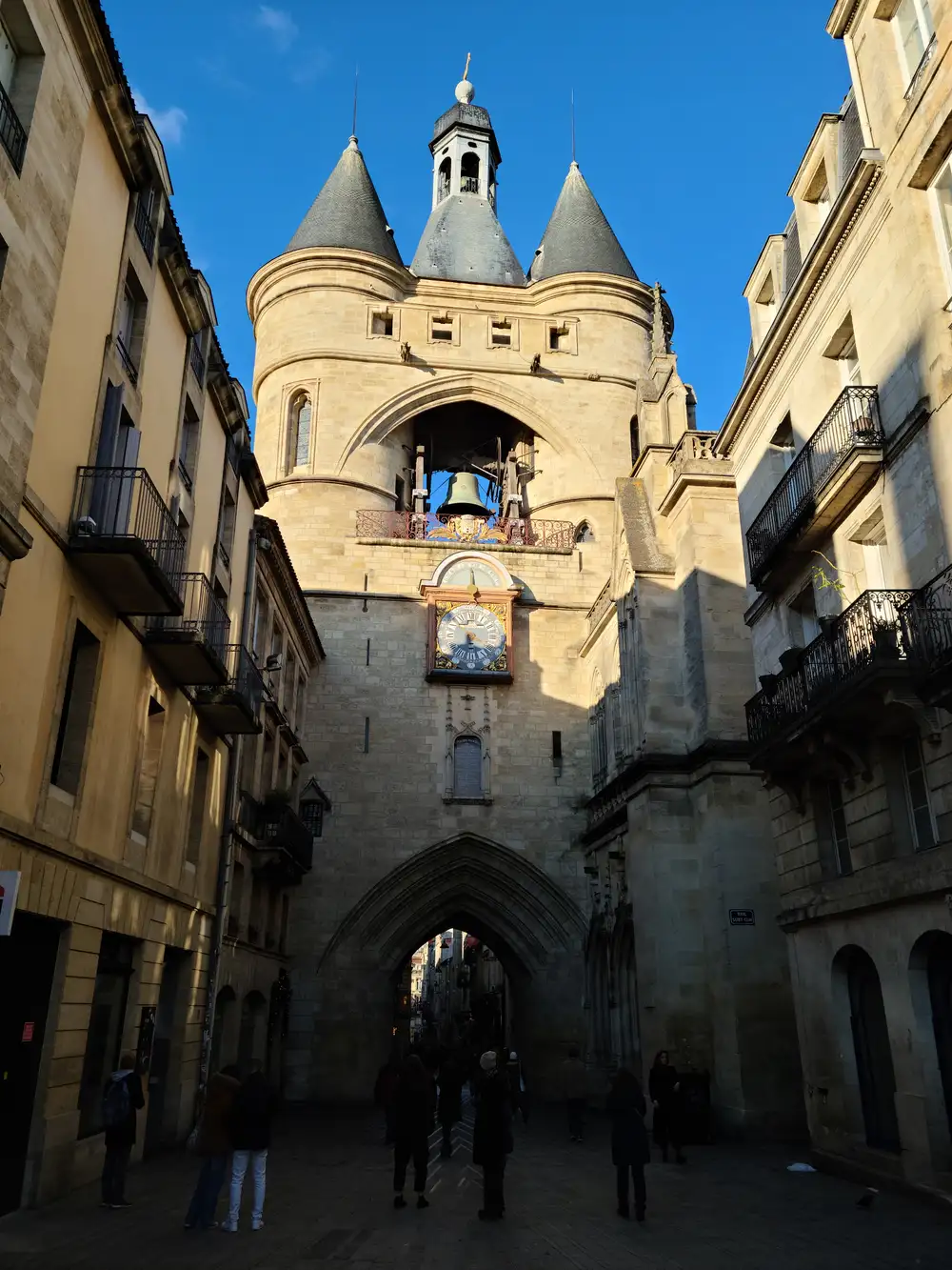 Front view of the Grosse Cloche gate's twin conical towers, central belfry, and zodiac clock framed by limestone buildings in Bordeaux