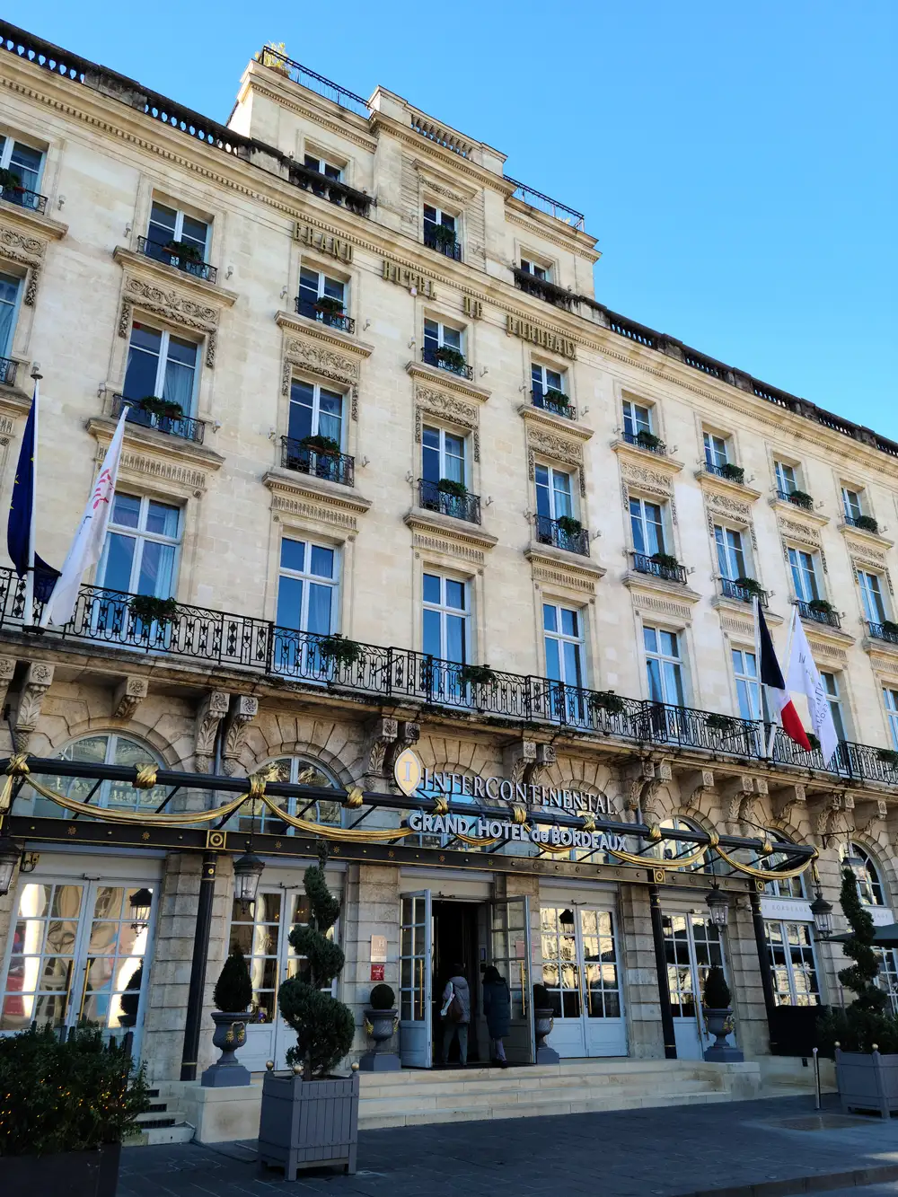 Ornate limestone facade and gilded canopy entrance of the InterContinental Grand Hôtel de Bordeaux under clear blue sky