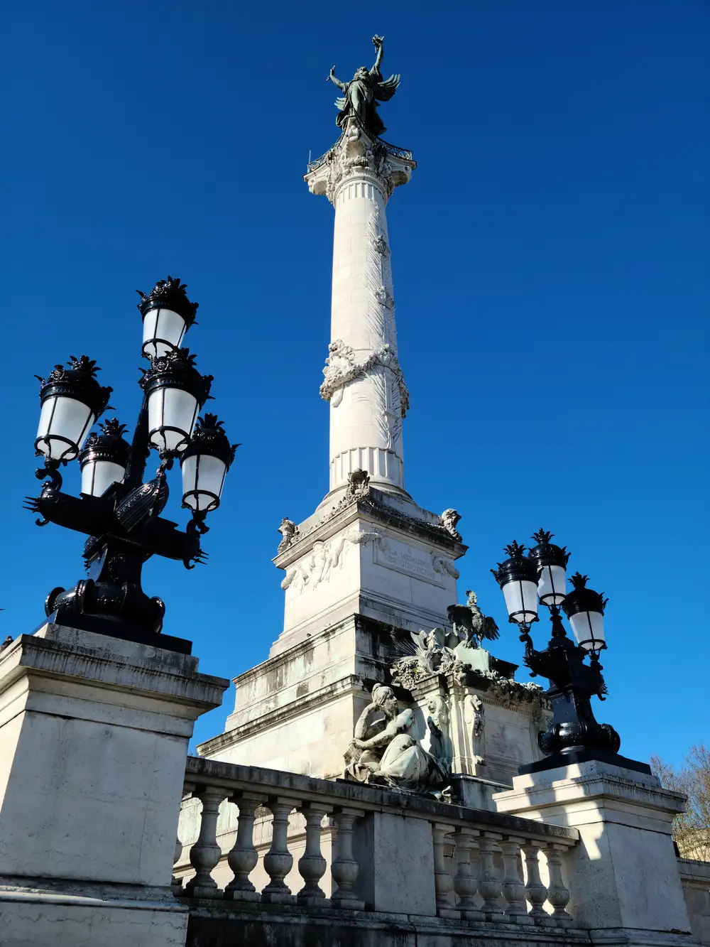 Monument aux Girondins column topped with Liberty statue beside ornate black lampposts under deep blue sky in Bordeaux