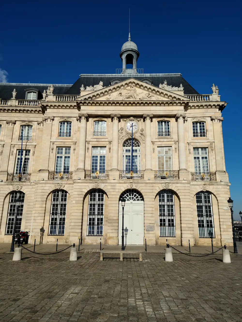 Central pavilion of the Palais de la Bourse with pediment sculptures, clock, and slate dome under deep blue Bordeaux sky