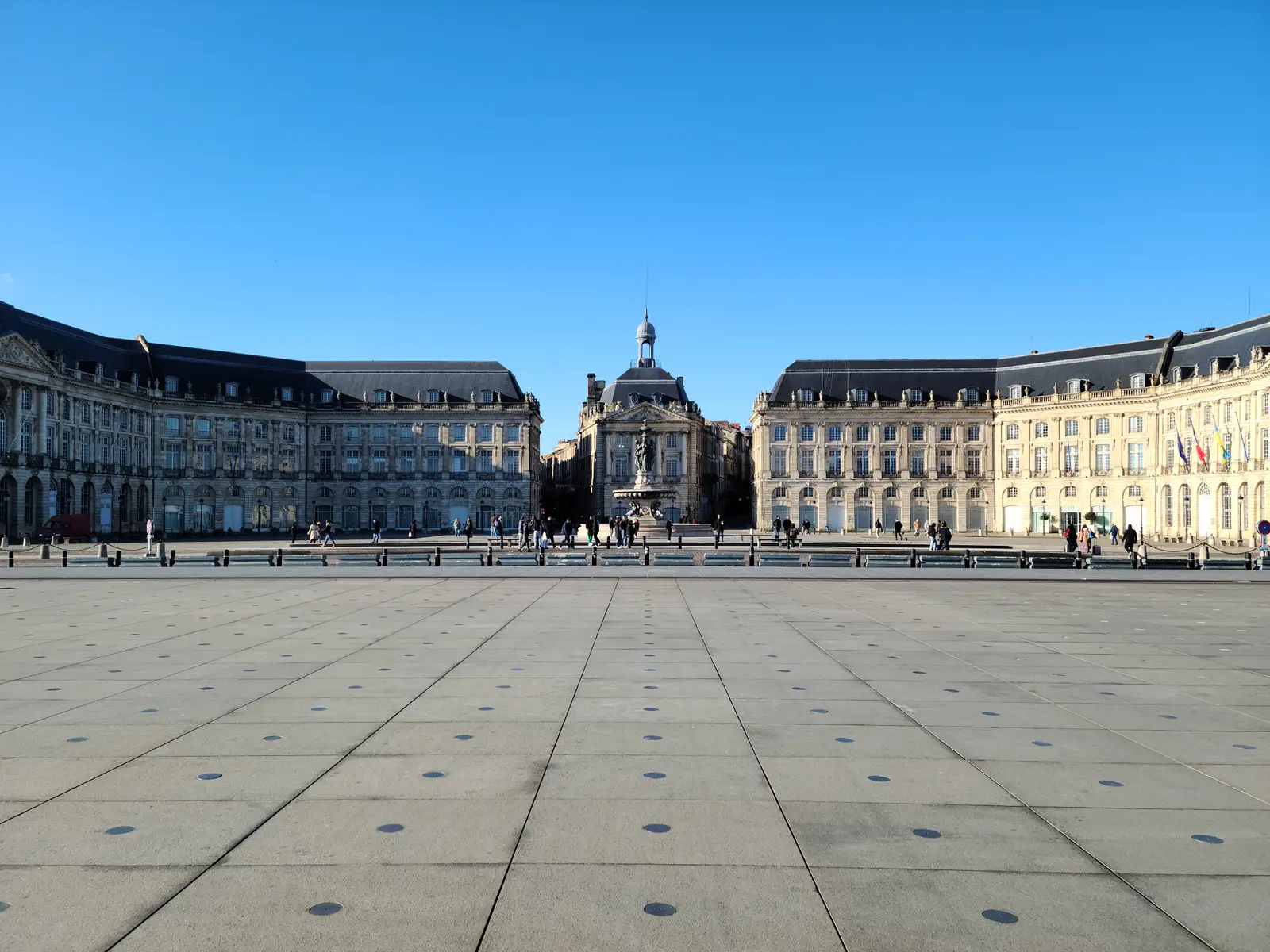 Place de la Bourse in Bordeaux with its Fountain of the Three Graces flanked by neoclassical facades under clear blue sky