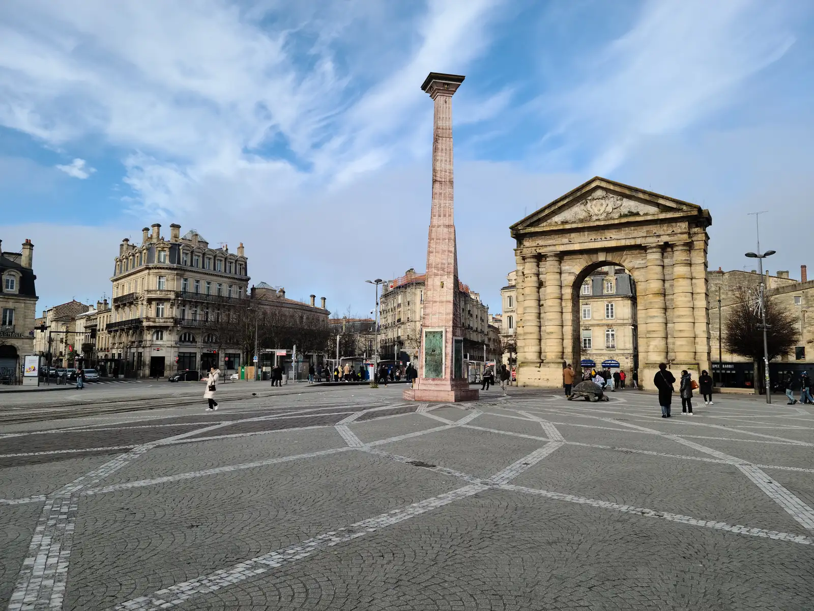 Pink marble obelisk rises beside the Porte d'Aquitaine arch across the wide cobblestone expanse of Place de la Victoire in Bordeaux