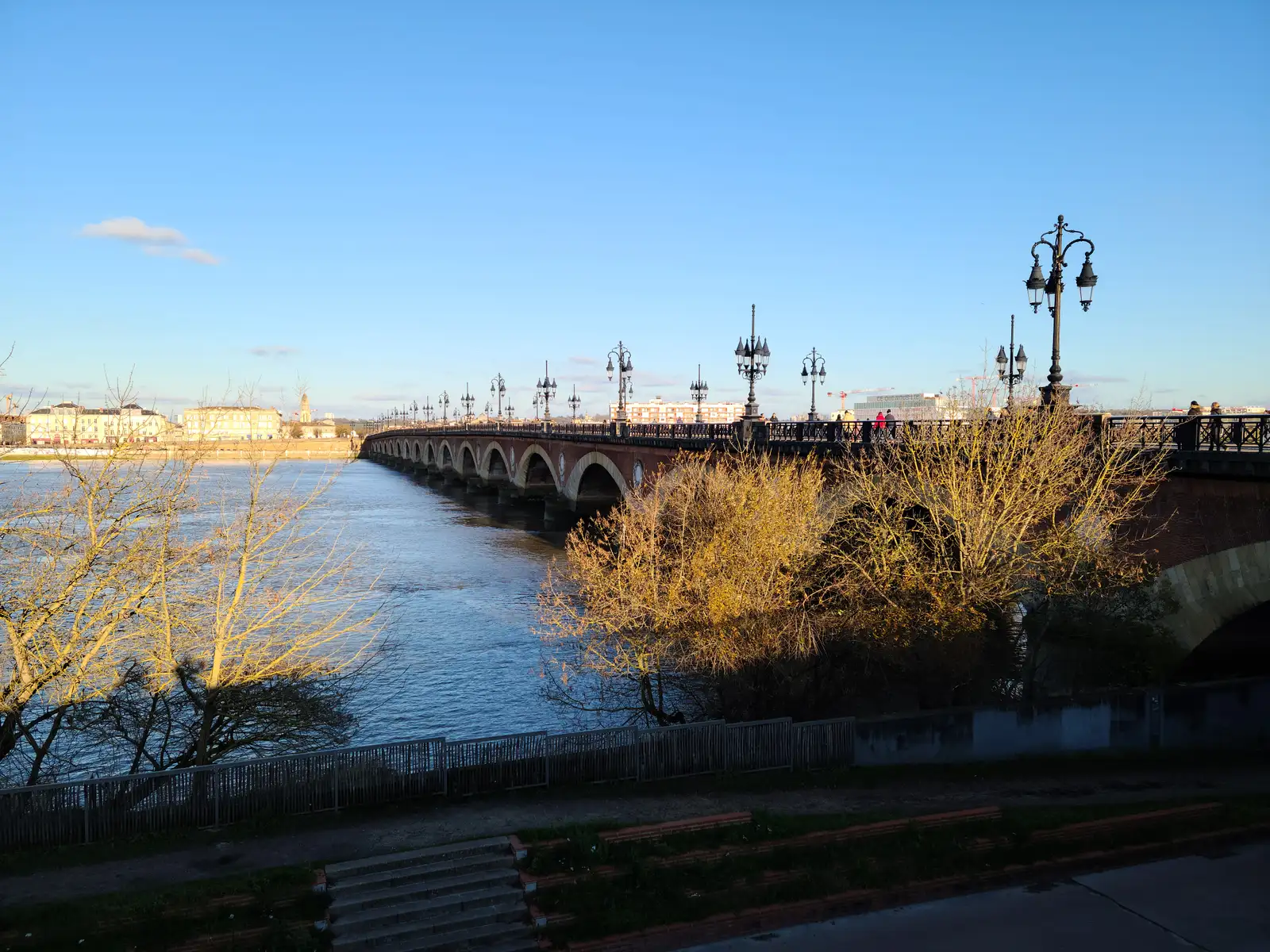 Golden afternoon light on Pont de Pierre's stone arches and ornate lampposts spanning the Garonne river in Bordeaux