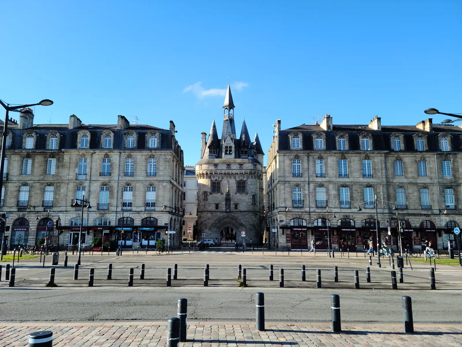 Porte Cailhau medieval gate framed by symmetrical stone buildings under blue skies in central Bordeaux