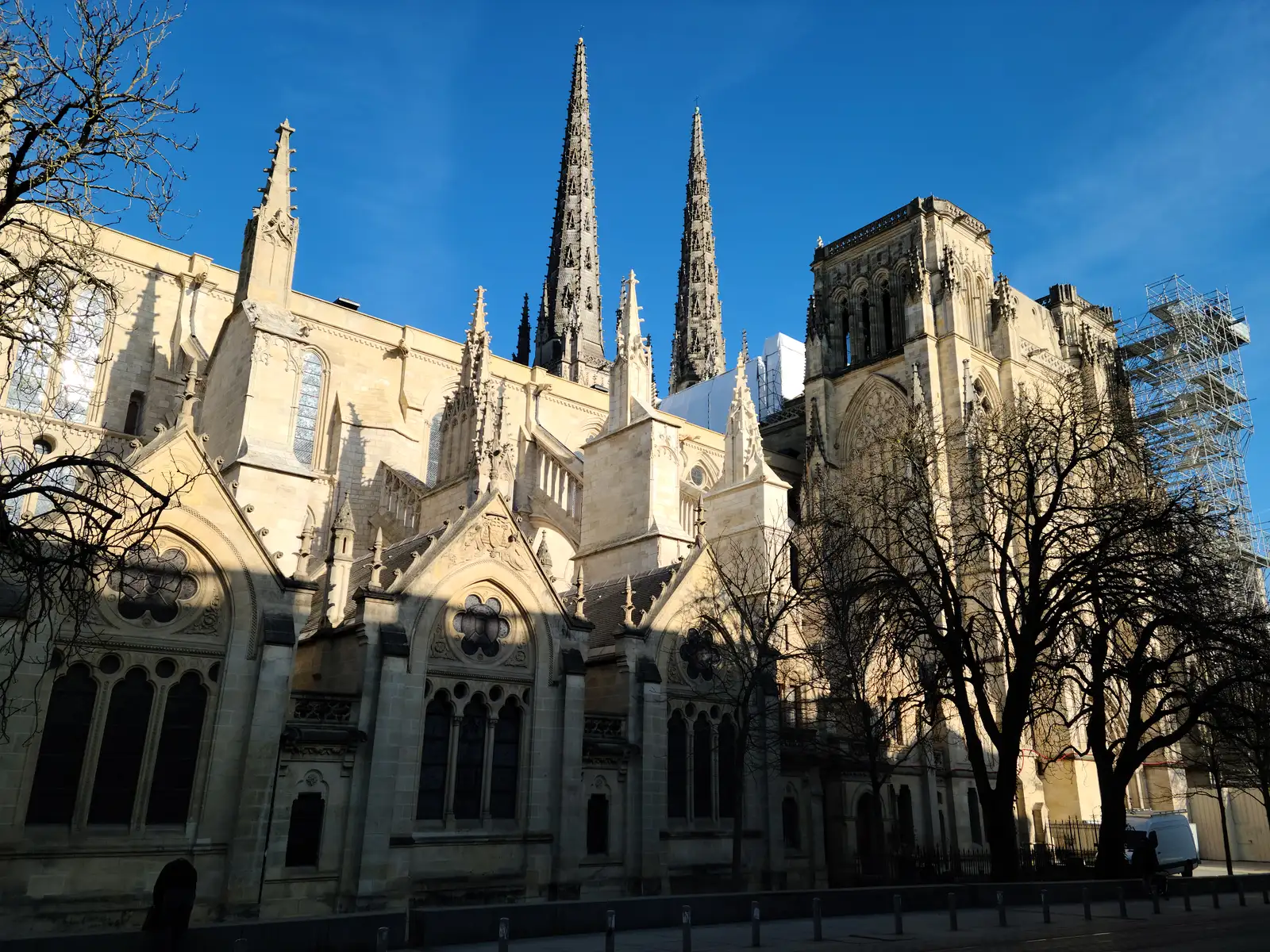 Flying buttresses and twin spires of Cathédrale Saint-André beside a scaffolded transept tower under blue Bordeaux sky