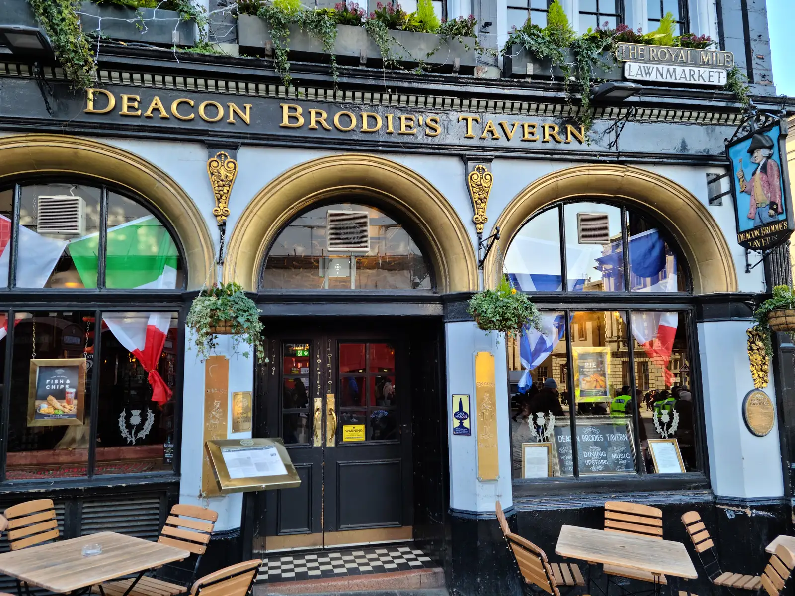 Ornate gold-lettered facade of Deacon Brodie's Tavern on the Royal Mile at Lawnmarket in Edinburgh with arched windows and flags