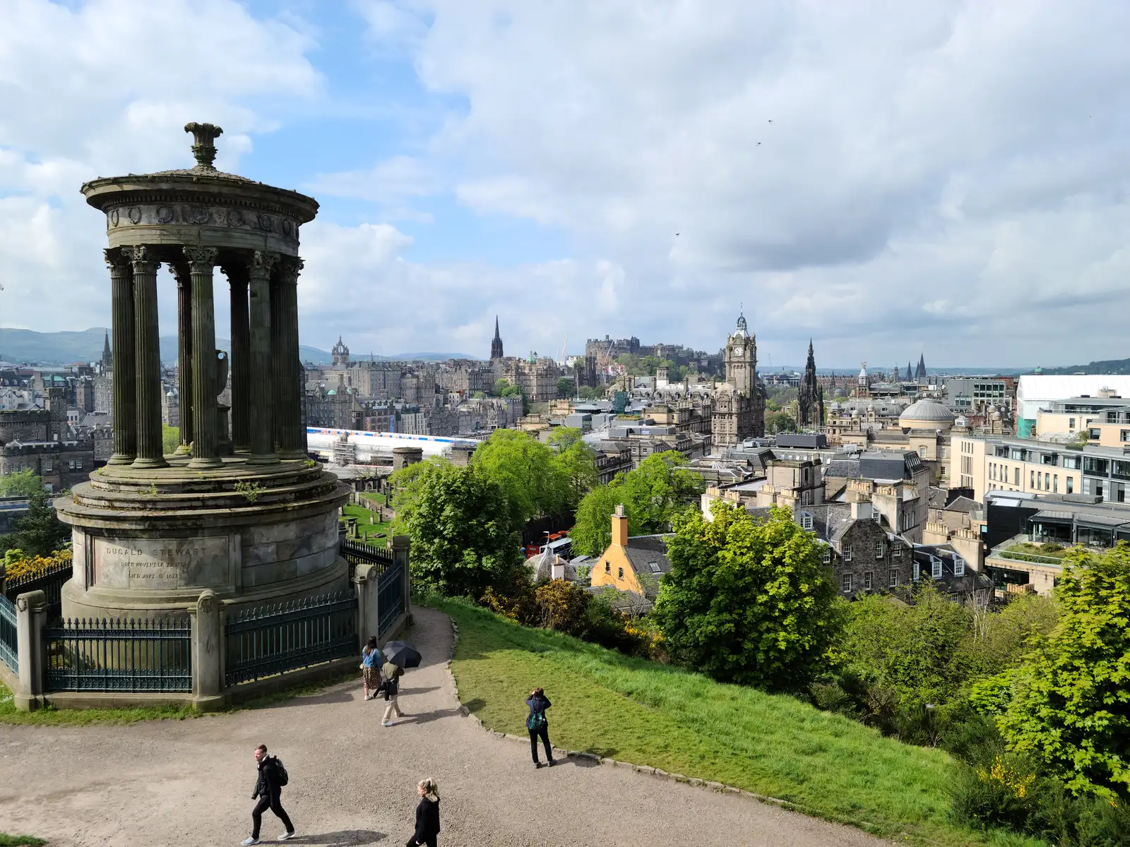 Dugald Stewart Monument's stone columns on Calton Hill above Edinburgh Old Town rooftops with Castle and Balmoral clock tower beyond