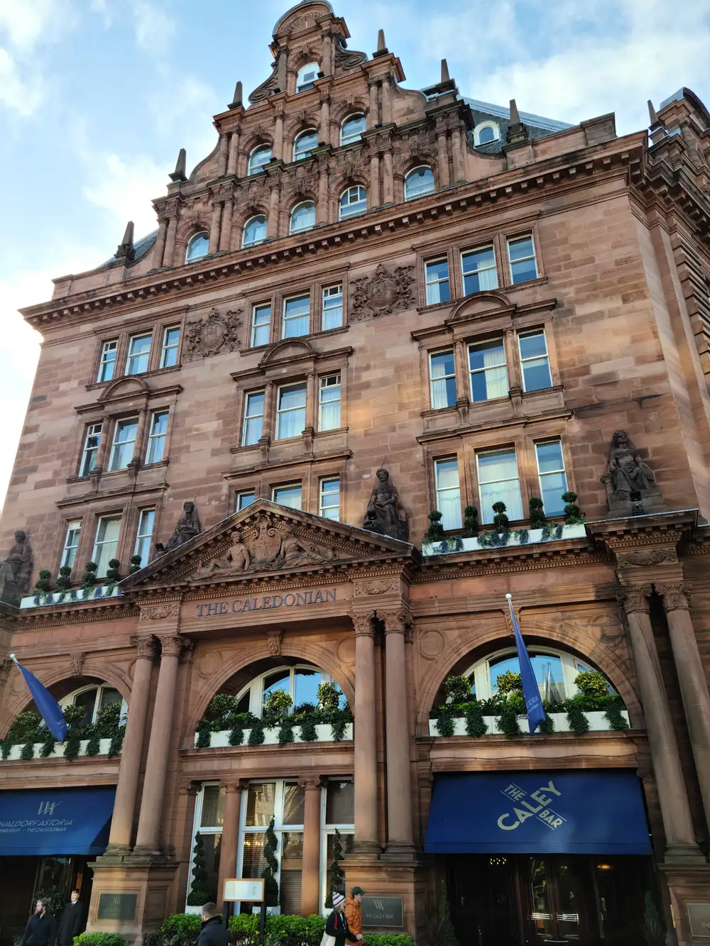 Ornate red sandstone facade of The Caledonian Waldorf Astoria hotel in Edinburgh with The Caley Bar awning below