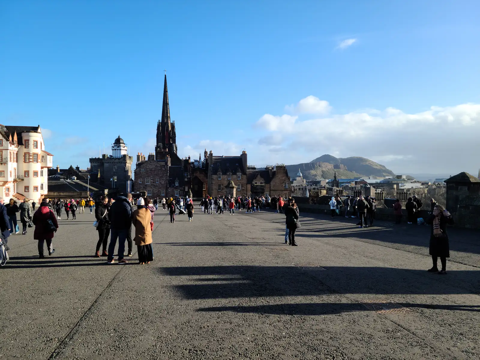 View east from Edinburgh Castle Esplanade towards Arthur's Seat and the Hub's spire with visitors in bright winter sunshine