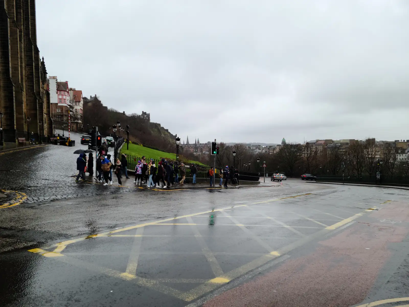 Tour group with umbrellas crossing Johnston Terrace below Edinburgh Castle esplanade on a rainy gray winter day