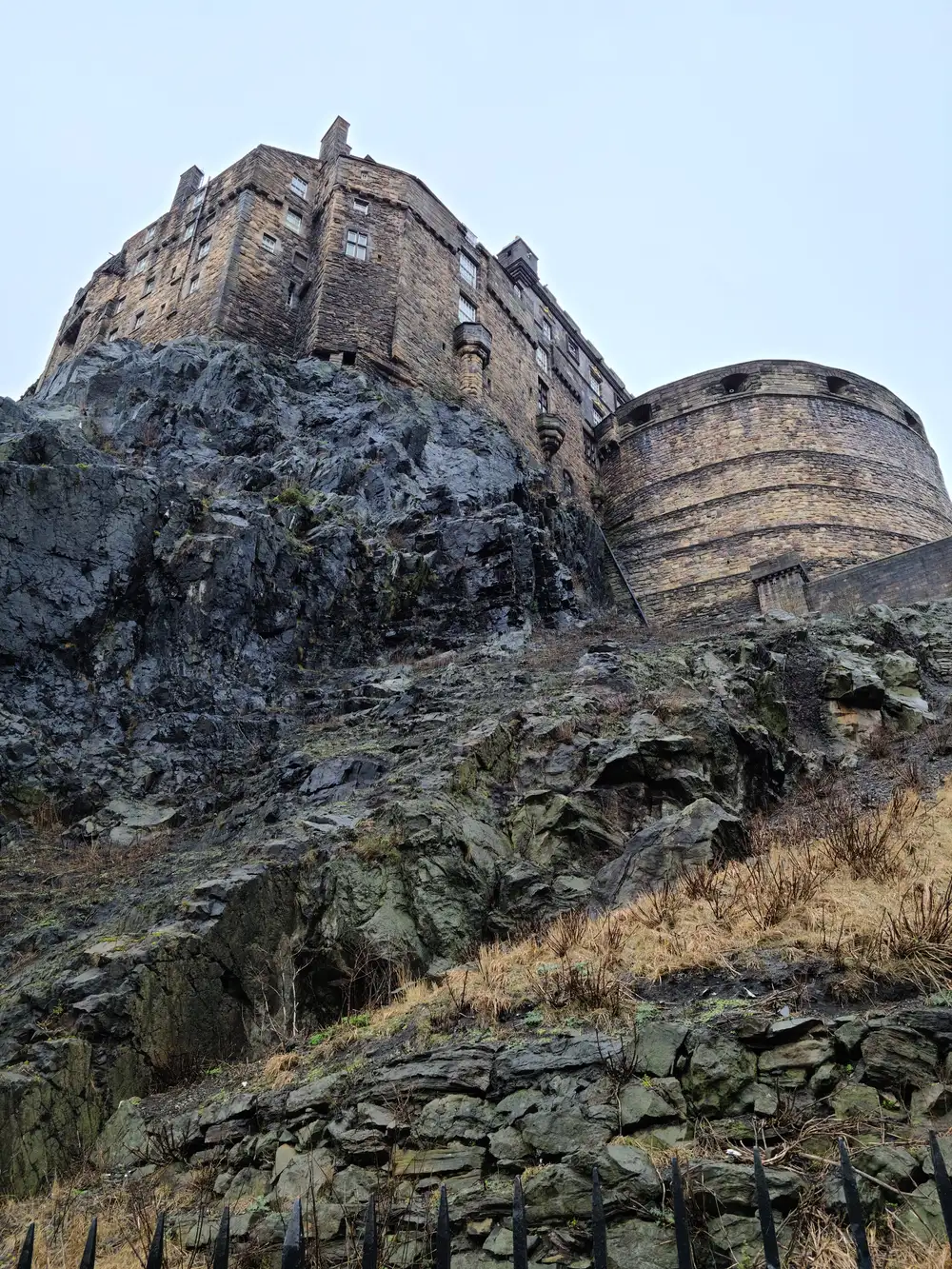 Vertiginous upward view of Edinburgh Castle's southern walls and round tower perched atop the sheer volcanic crag in winter