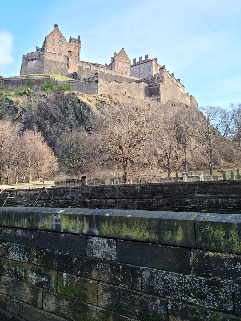 Edinburgh Castle rising on its volcanic crag above Waverley Station walls and bare winter trees from Princes Street Gardens