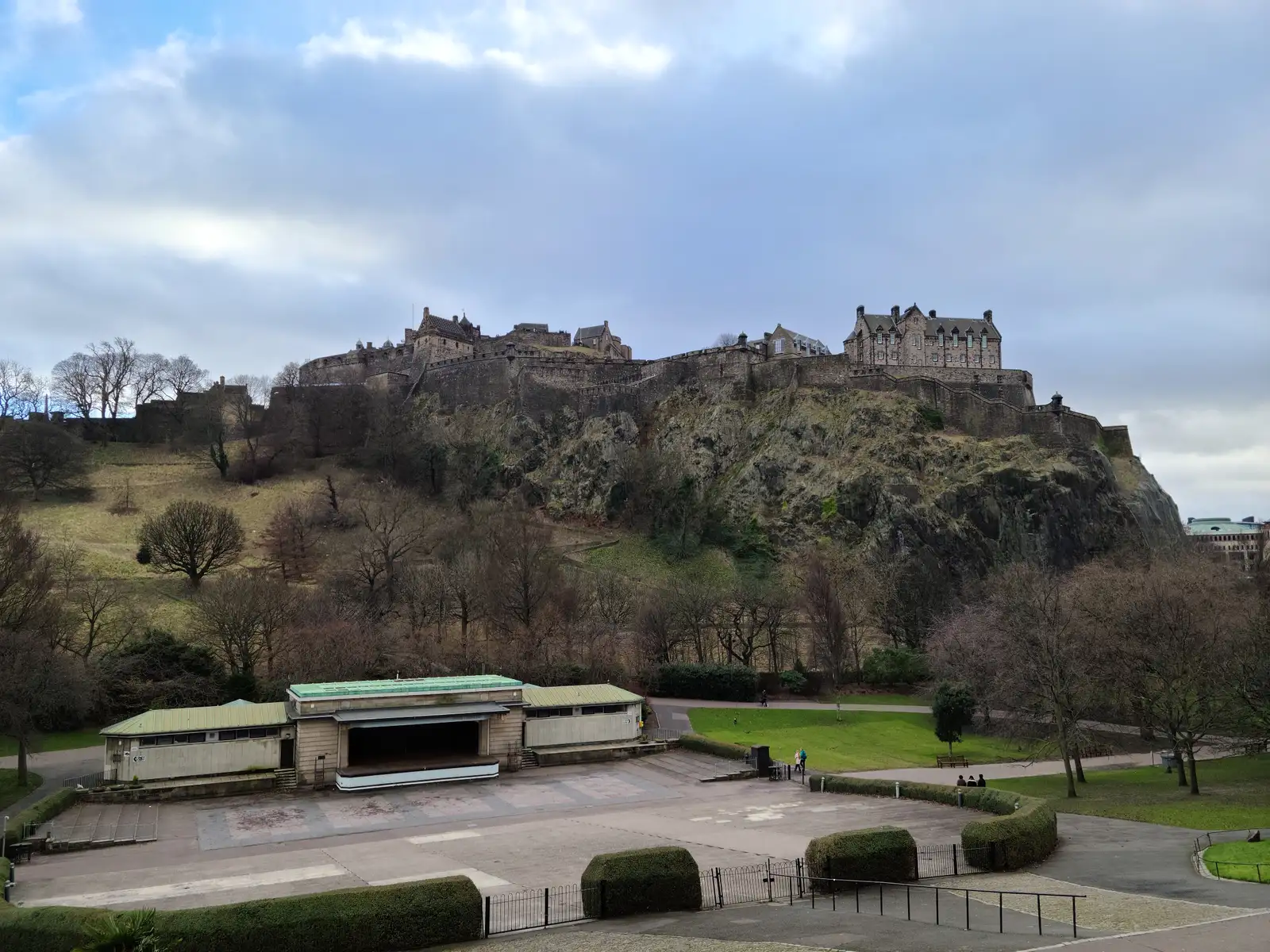 Edinburgh Castle on its volcanic crag above the Ross Bandstand stage in West Princes Street Gardens under cloudy winter sky