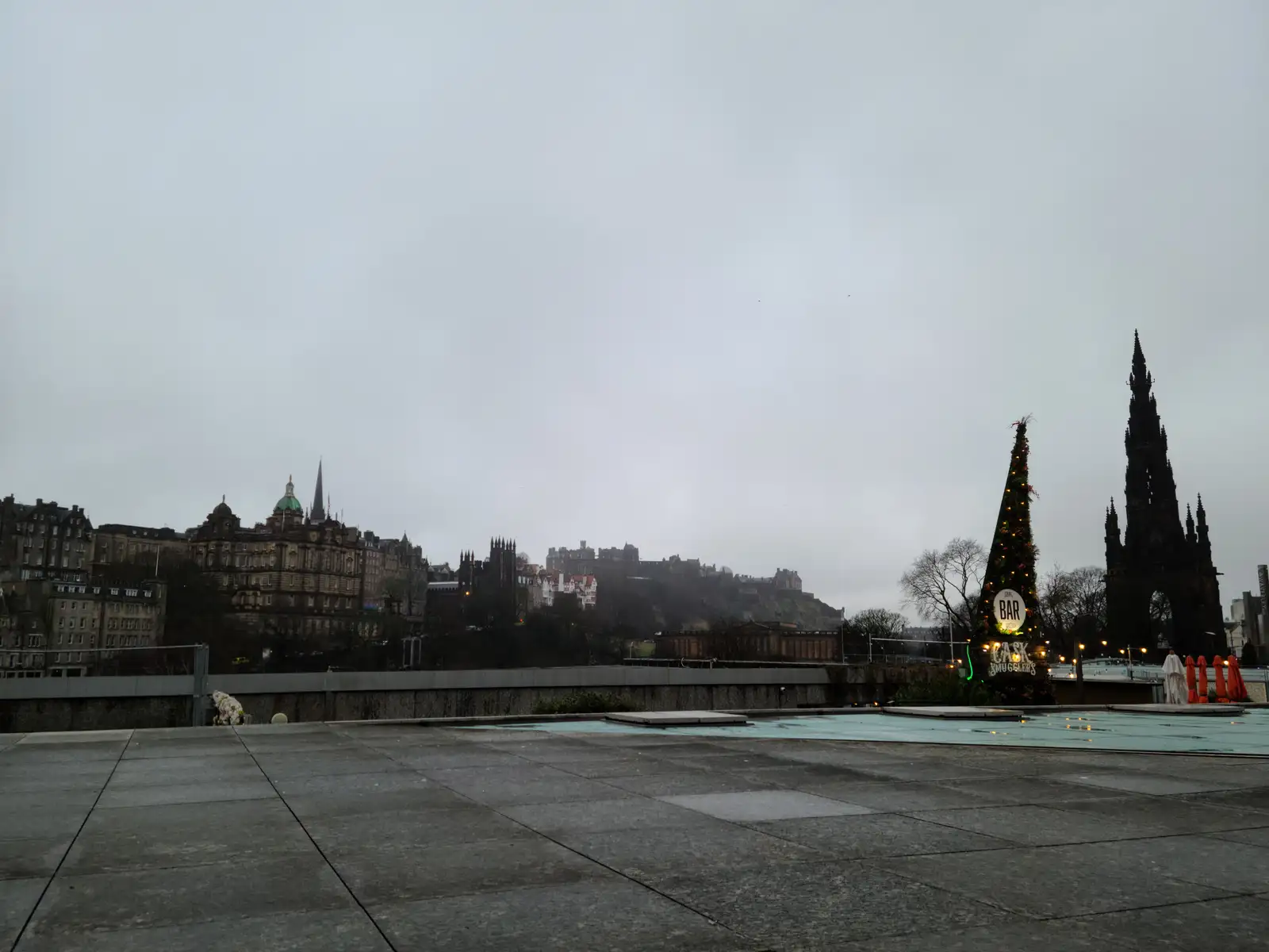 Panoramic view from a museum rooftop terrace of Edinburgh Castle on its crag, Bank of Scotland dome and Scott Monument under gray skies