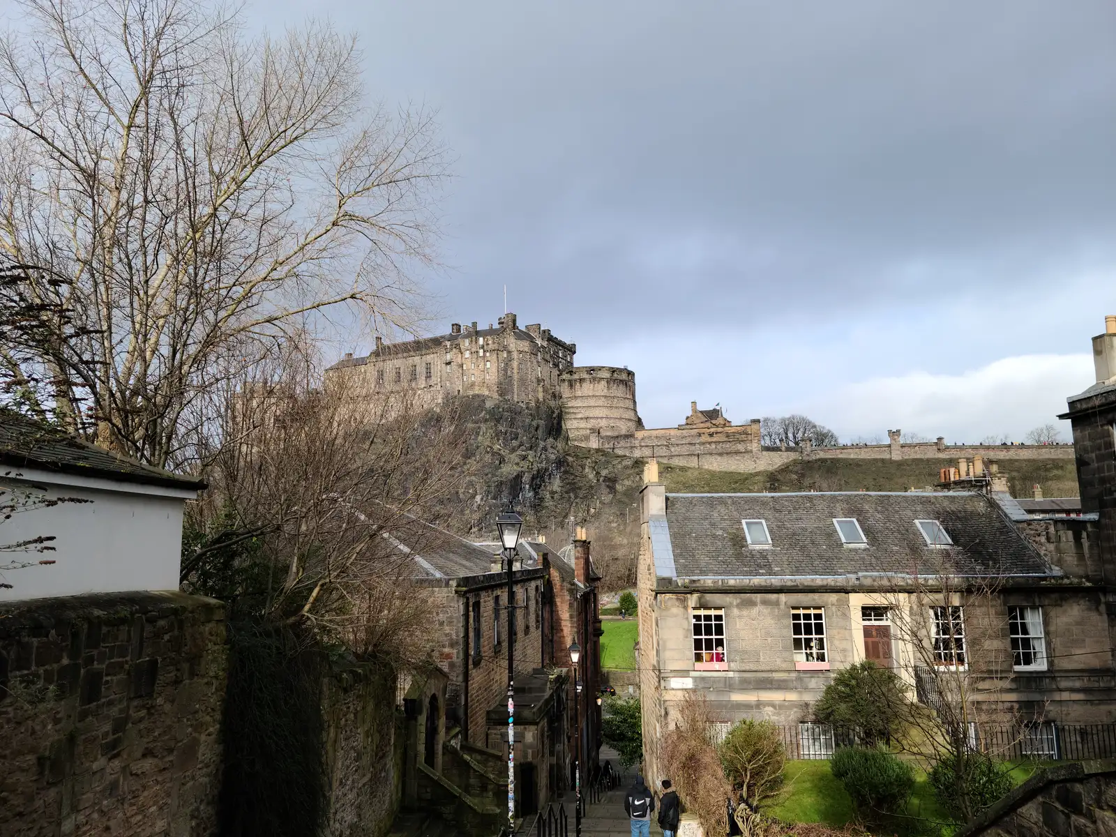 View of Edinburgh Castle on its crag from the Vennel steps with sandstone tenement rooftops and bare winter trees in the foreground