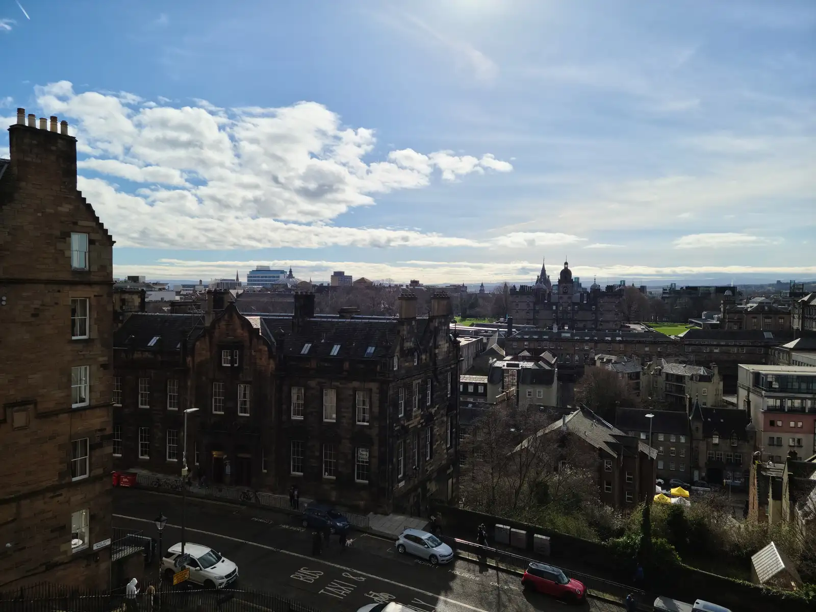 Elevated view across Edinburgh Old Town tenement rooftops towards the Firth of Forth and distant skyline under blue winter sky