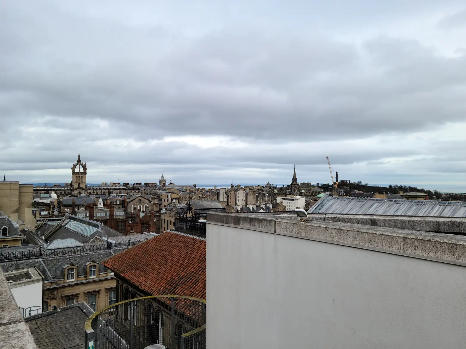 Edinburgh Old Town skyline with Tron Kirk and Tolbooth Kirk spires rising above rooftops viewed from a museum terrace under gray skies