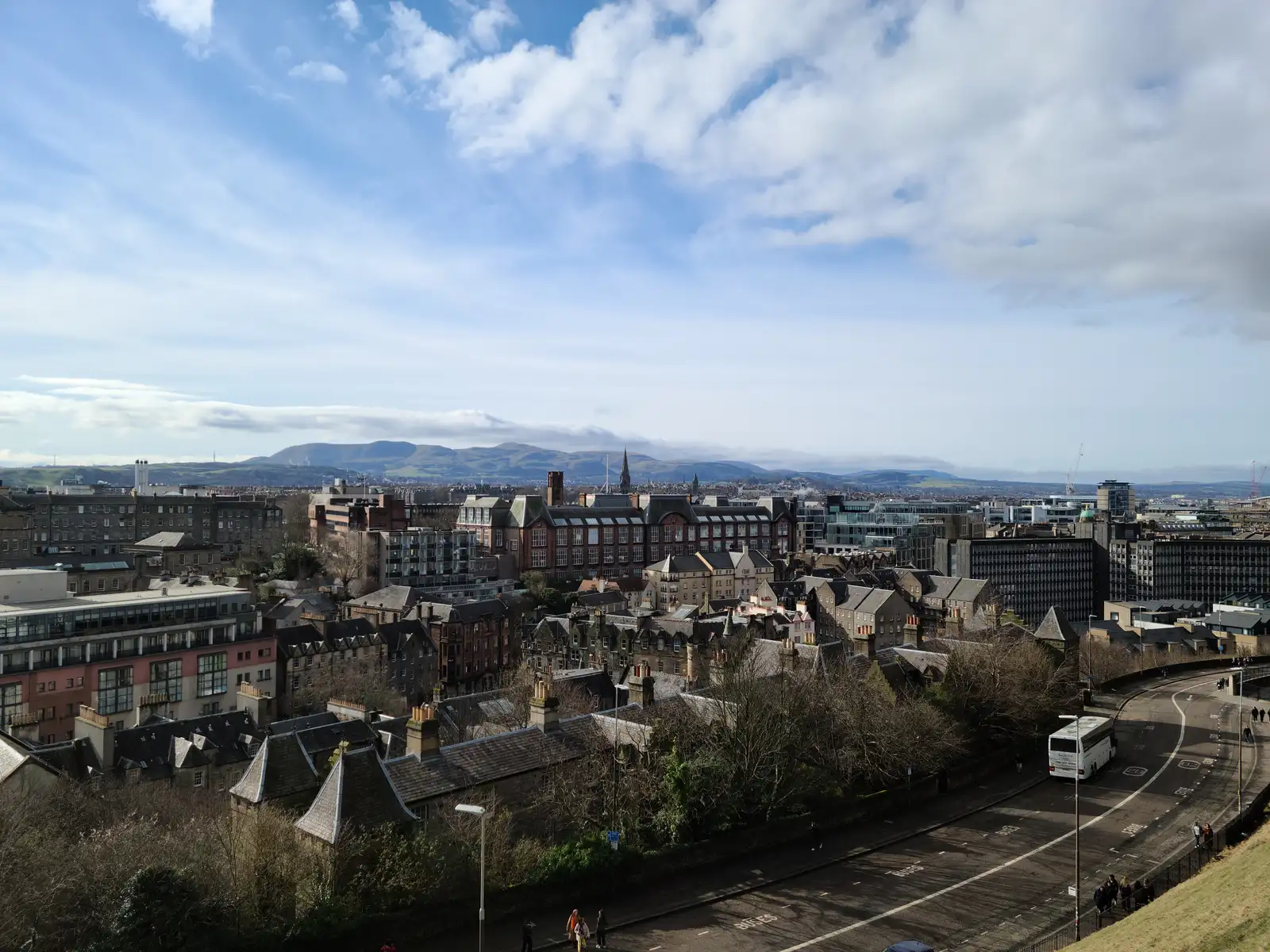 View across Edinburgh's southern rooftops and Newington tenements towards the Pentland Hills under a bright cloud-streaked sky