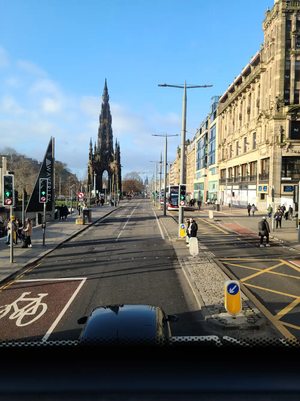 View from a bus on Edinburgh's Princes Street with the Waverley Station sign, tram tracks and Scott Monument ahead