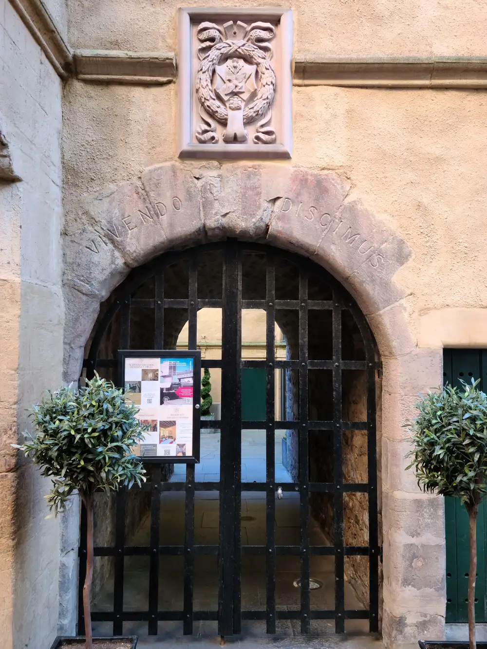 Wrought iron gate beneath the Vivendo Discimus stone arch and carved crest at the entrance to Riddle's Court off the Royal Mile