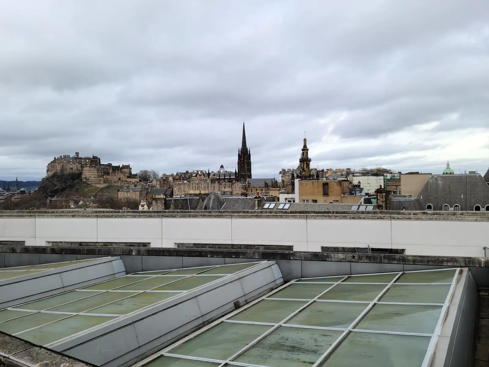 View across museum rooftop skylights to Edinburgh Castle, Tolbooth Kirk spire and Old Town skyline under gray winter skies