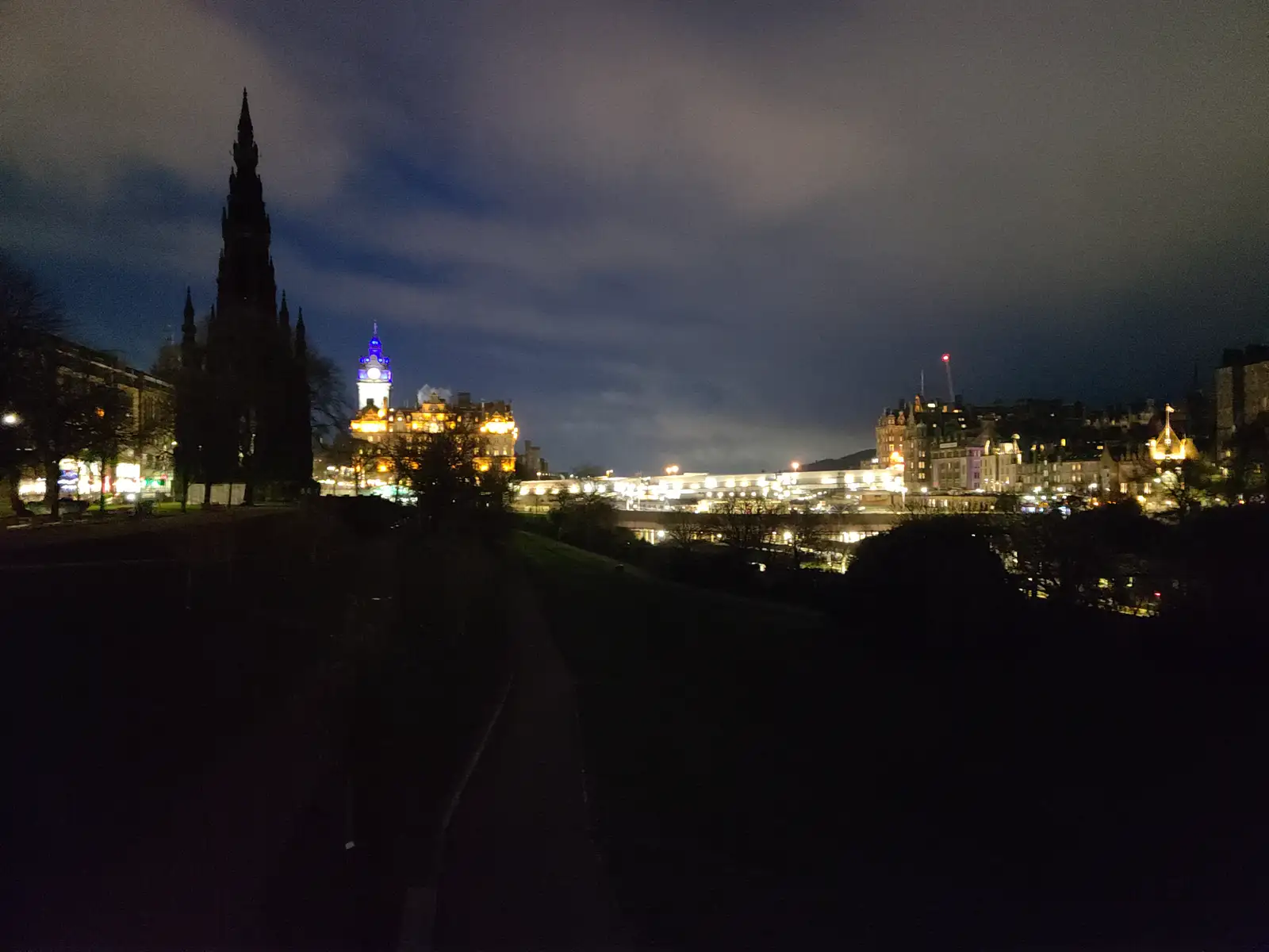Floodlit Scott Monument and Balmoral Hotel clock tower silhouetted against Edinburgh's Old Town skyline at night from Princes Street Gardens
