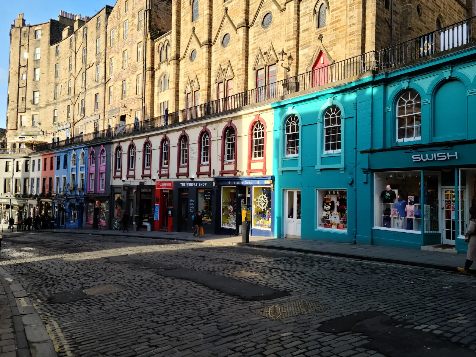 Curving row of colorful shopfronts on Victoria Street in Edinburgh Old Town with turquoise Swish store and cobbled road