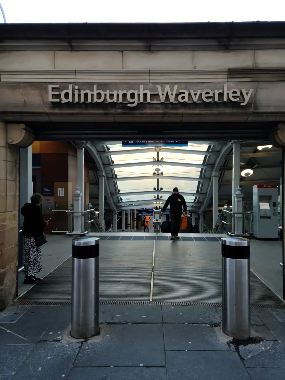 Edinburgh Waverley railway station entrance with carved sandstone sign, steel bollards and glass canopy over the ramp down to platforms