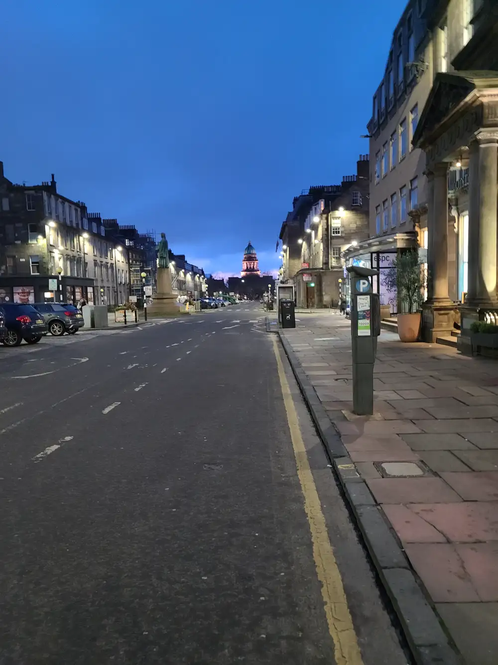 West Register House's illuminated dome rising at the end of George Street in Edinburgh at dusk with parked cars and tenements