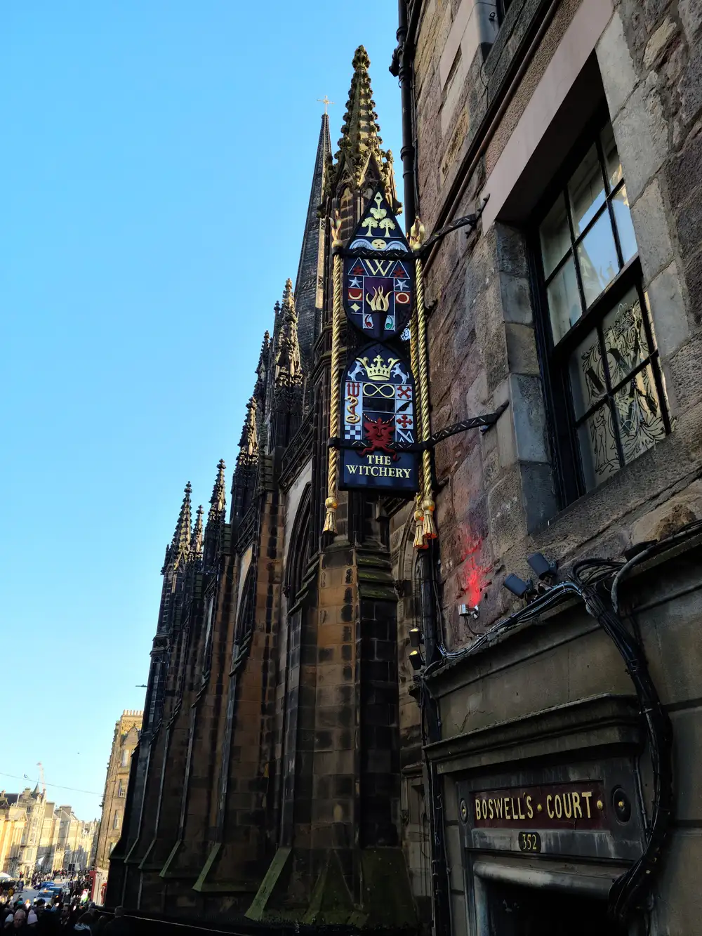 Ornate hanging sign for The Witchery restaurant beside Boswell's Court entrance and the Hub's gothic spire on Castlehill in Edinburgh