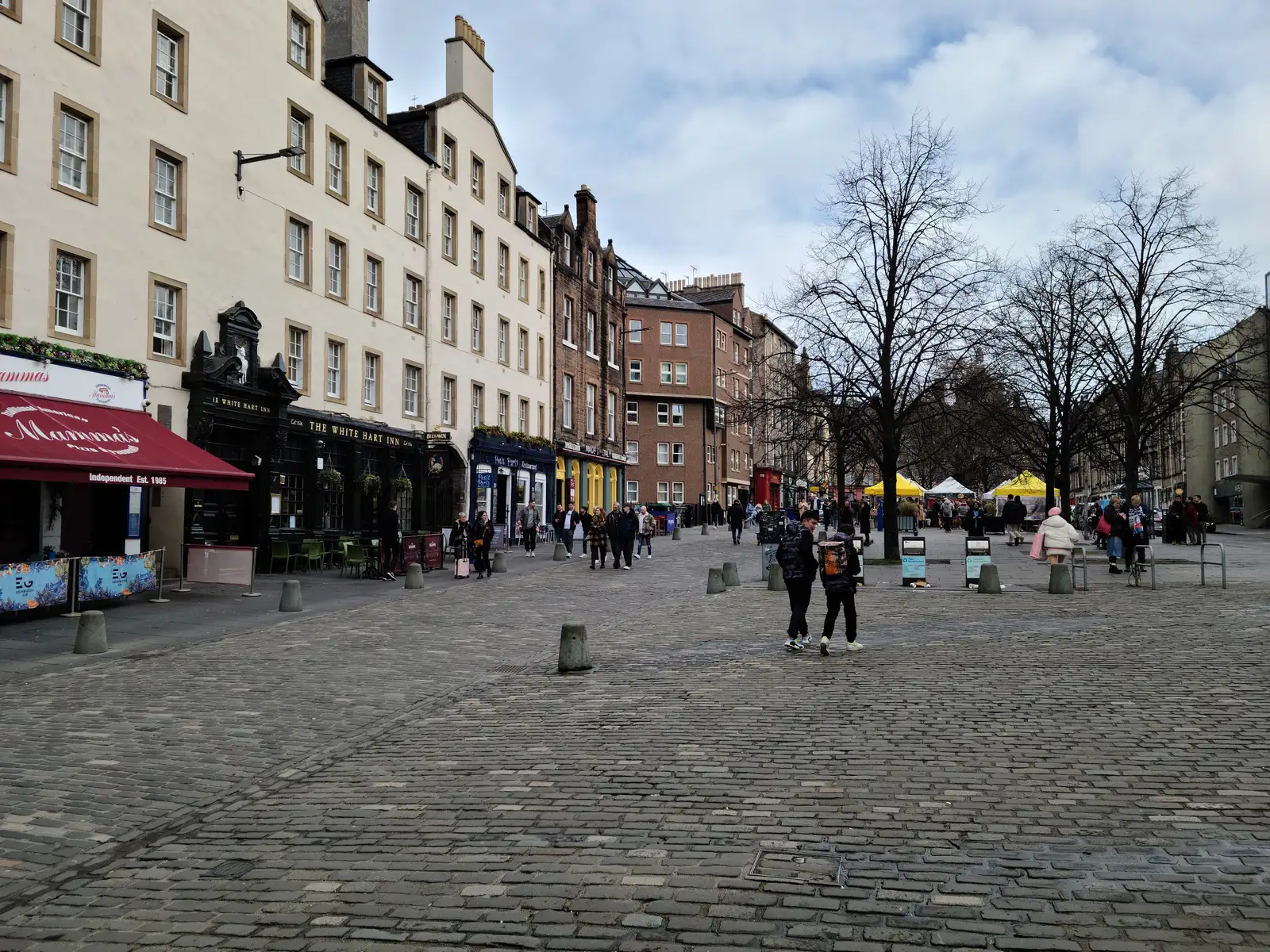 Cobbled Grassmarket square in Edinburgh Old Town with The White Hart Inn pub and Mamma's red awning beneath tenements