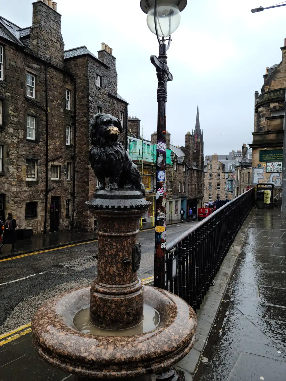 Bronze statue of Greyfriars Bobby the Skye terrier on his granite fountain plinth at Candlemaker Row in Edinburgh on a rainy day