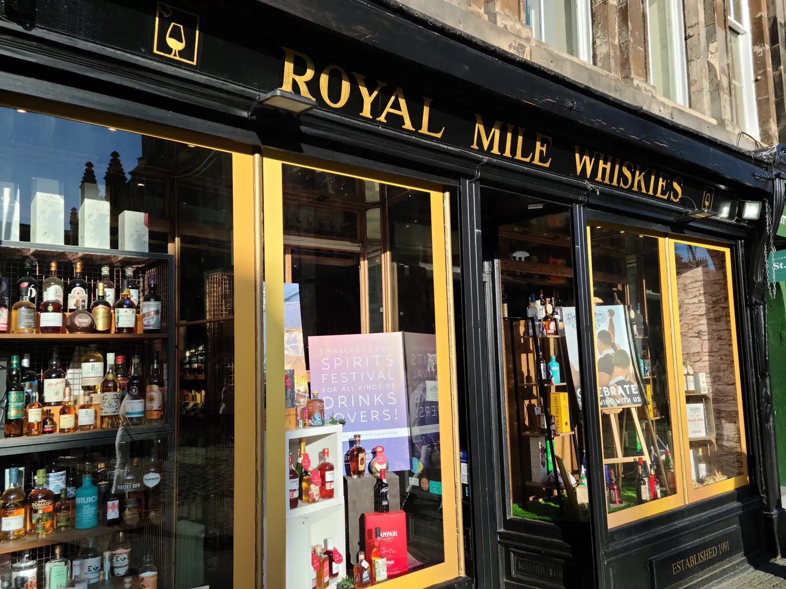 Royal Mile Whiskies shop front in Edinburgh with gold lettering on black facade and window display of spirits and whisky bottles