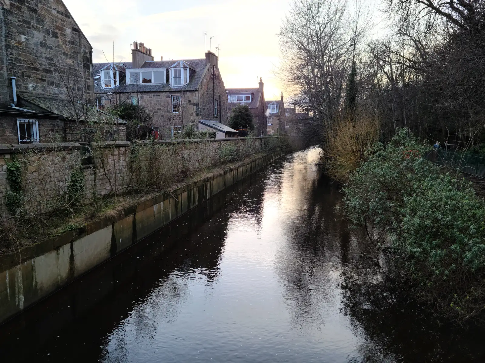 Water of Leith flowing past stone retaining walls and Dean Village tenements with sunset reflections on the river in Edinburgh