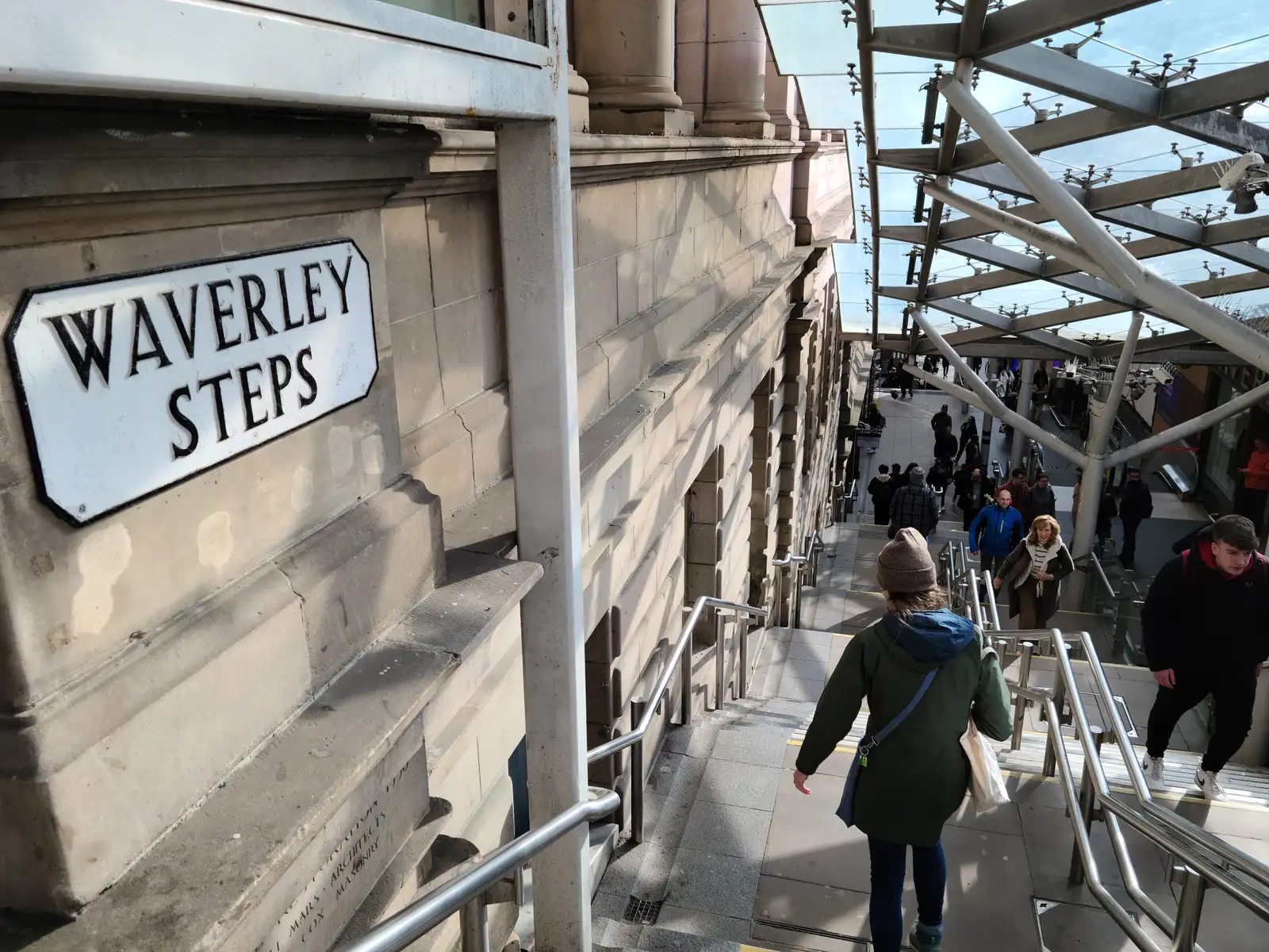 Cast iron Waverley Steps sign on sandstone wall above the steps leading down to Edinburgh Waverley Station's glass canopy