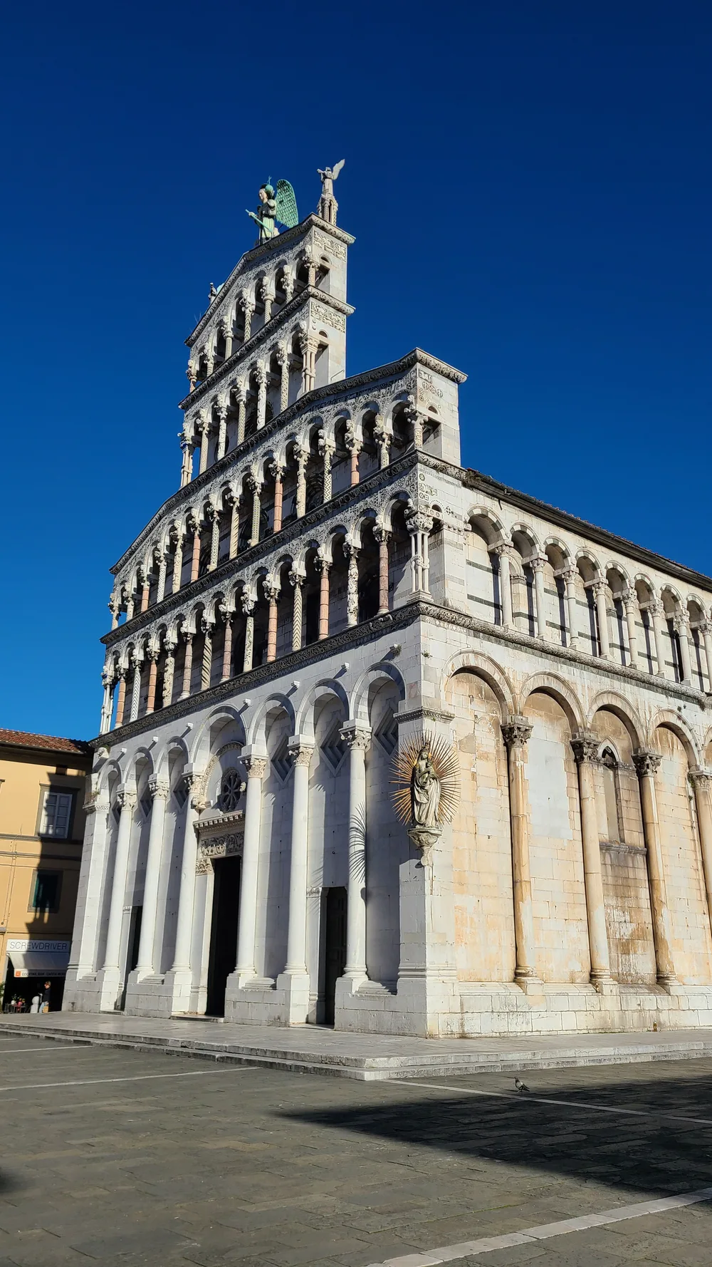 Full Pisan Romanesque marble facade of Chiesa di San Michele in Foro in Lucca, stacked tiers of blind arcades and marble columns rising against a deep blue sky