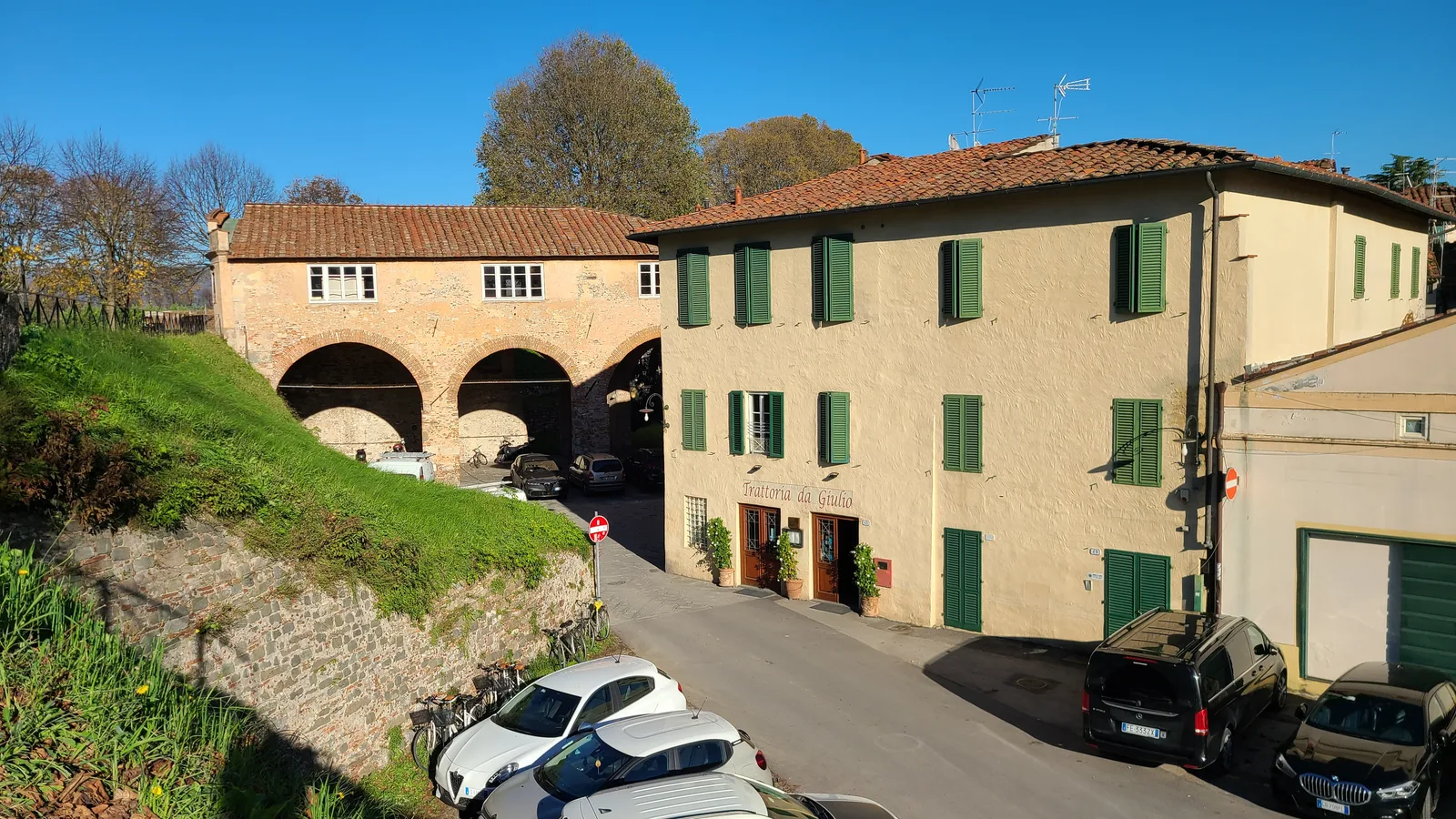 Triple stone arched gate in Lucca's city walls with an ochre residential building with green shutters alongside, viewed from outside the walls