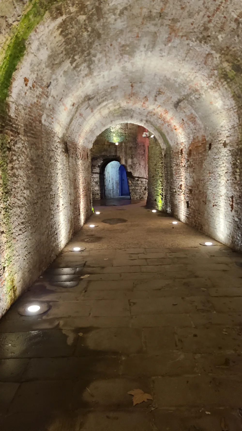 Long vaulted brick tunnel passage inside Lucca's city walls, lit by warm floor lights with a series of barrel-vaulted arches receding into the distance
