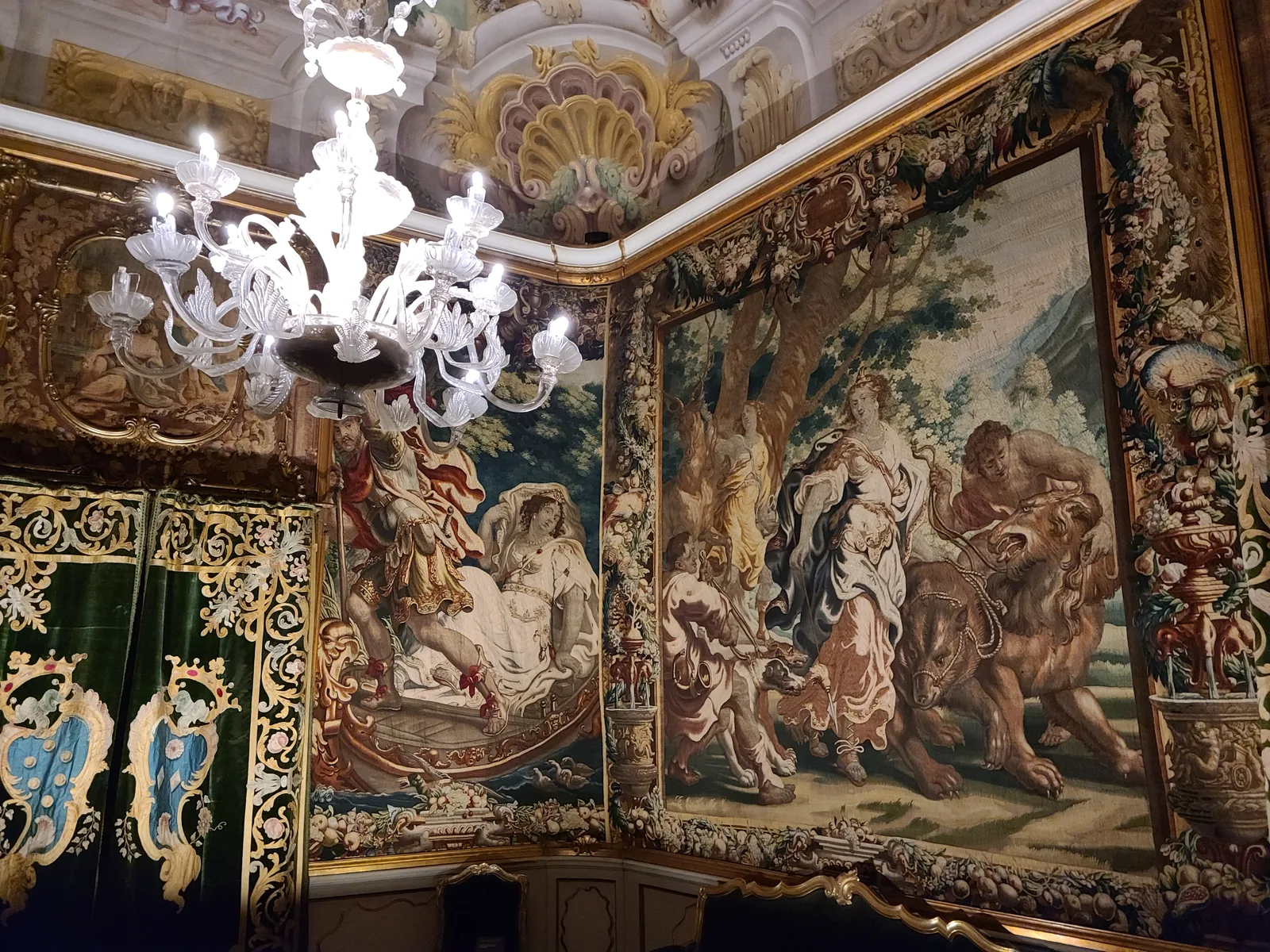 Room in a Lucca palazzo with a large Flemish tapestry depicting mythological figures covering the wall, a Murano glass chandelier, and gold ornamental wall details