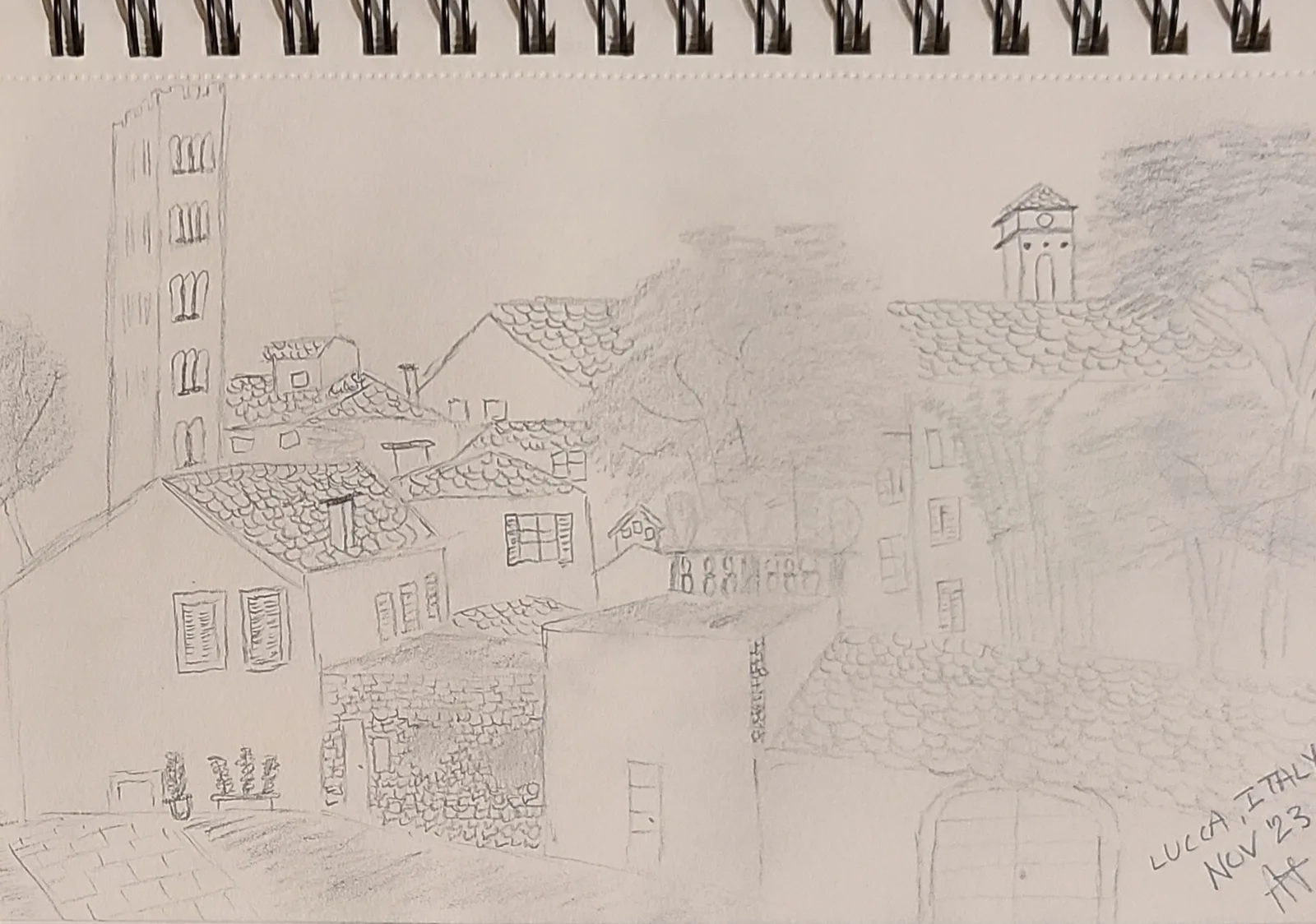Hand-drawn pencil sketch in a spiral sketchbook showing Lucca's terracotta rooftops and medieval towers, inscribed Lucca Italy Nov 23