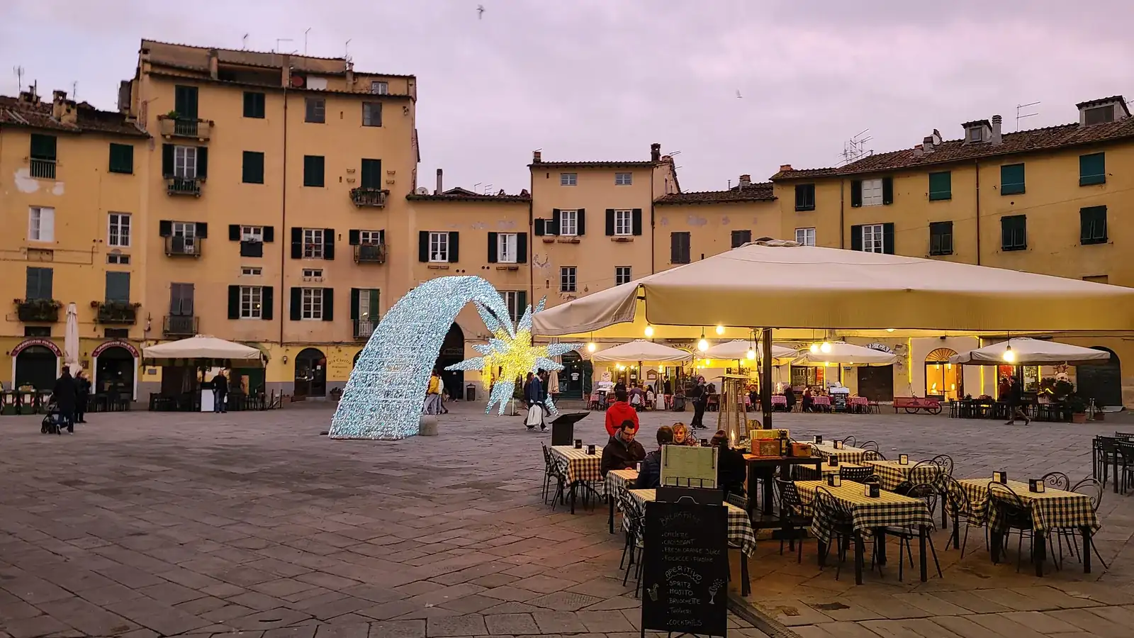 Piazza dell'Anfiteatro in Lucca at dusk, with cafes lit up around the perfectly oval medieval piazza