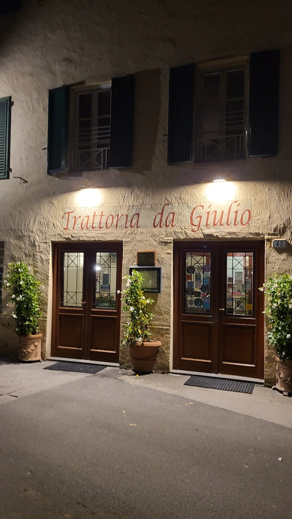 Trattoria da Giulio restaurant exterior at night in Lucca, warm lights illuminating the stone facade with the name in red lettering above wooden doors